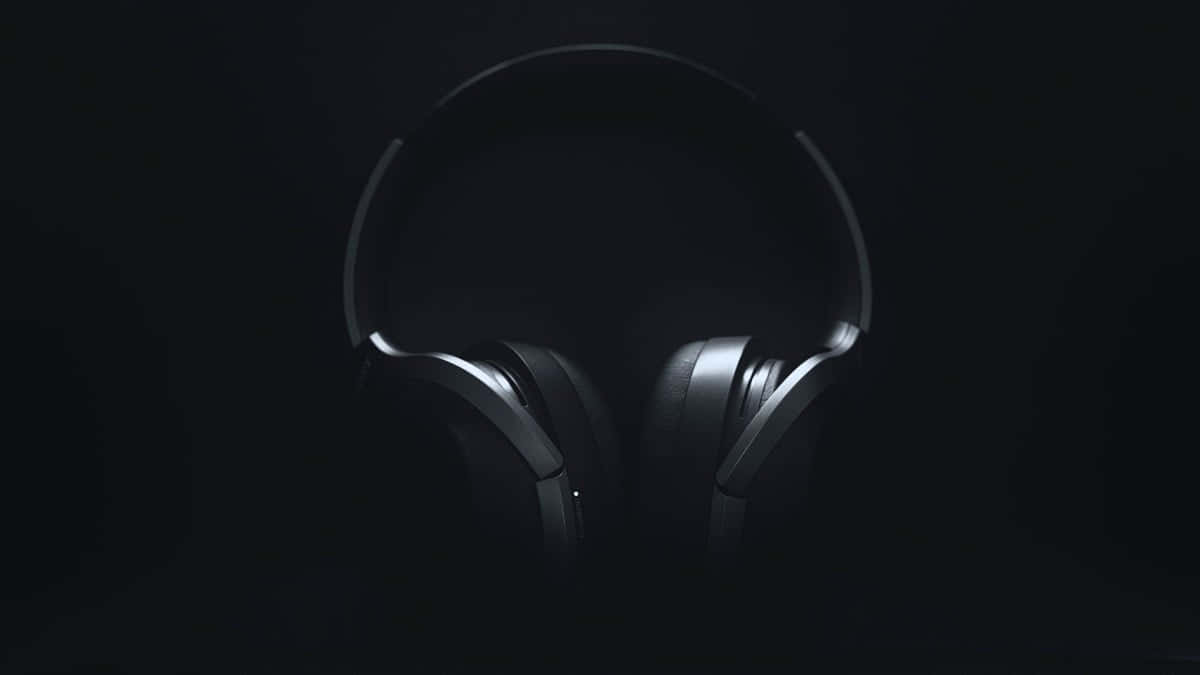 Headphones 桌布 壁紙 — 時尚黑色頭戴式耳機在漆黑背景中，以戲劇性的低調燈光微微發光。