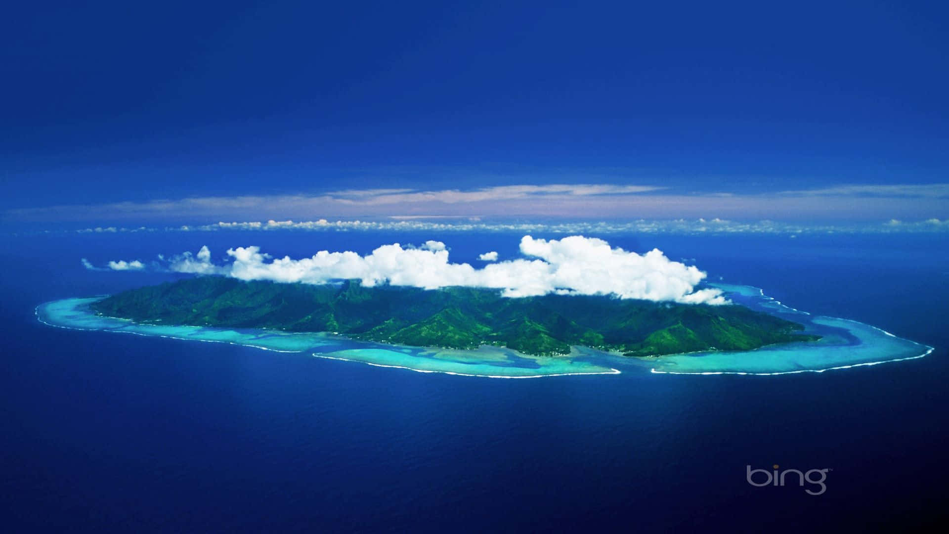 必應 桌布 壁紙 — 晴朗天空下，一個鬱鬱蔥蔥的綠色熱帶島嶼被充滿活力的綠松石色潟湖和深藍色海洋包圍的鳥瞰圖。