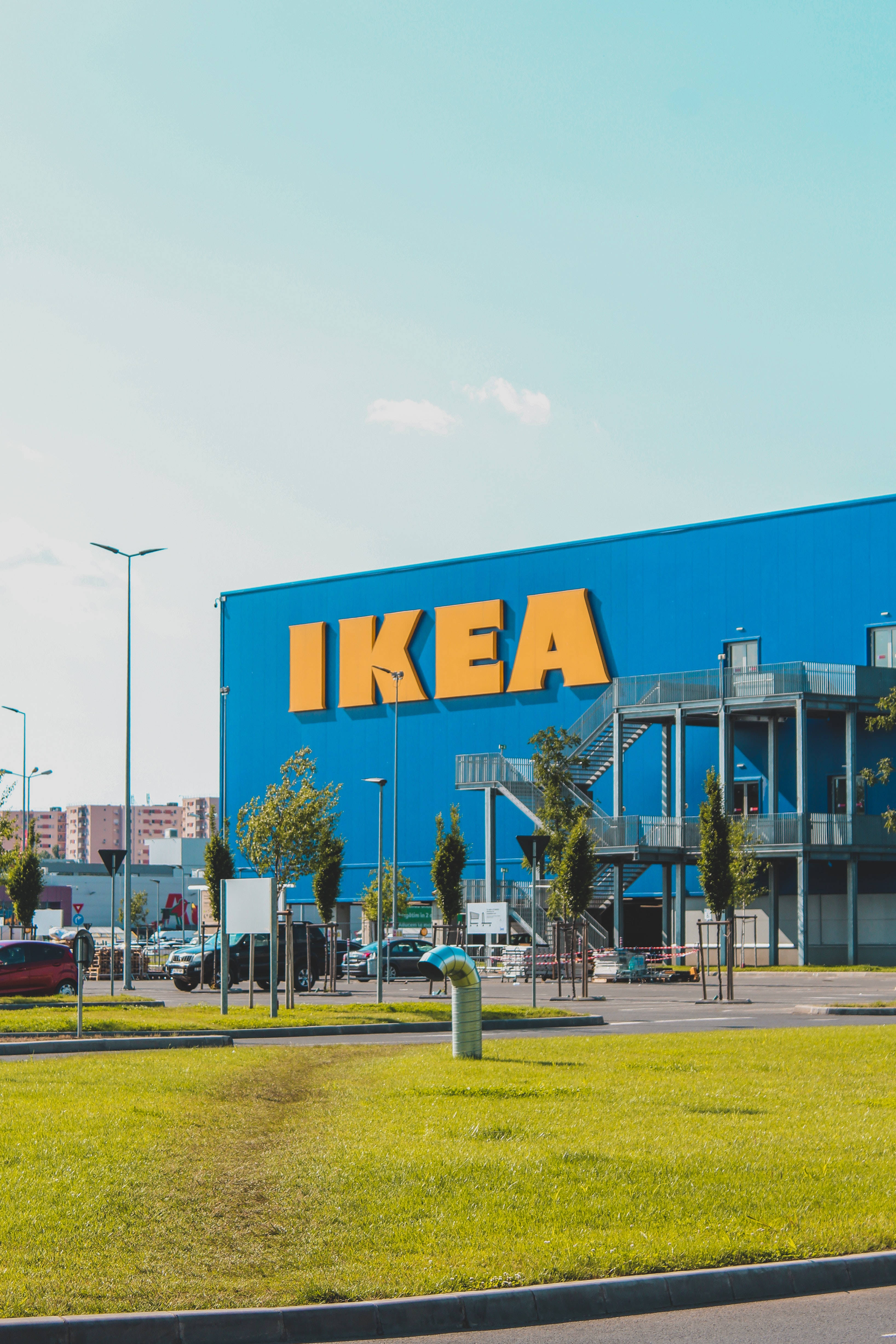 Sweden 桌布 壁紙 — 晴朗天空下，一座明亮的藍色IKEA商店建築，帶有醒目的黃色標誌，周圍環繞著綠色草地和停放的汽車。