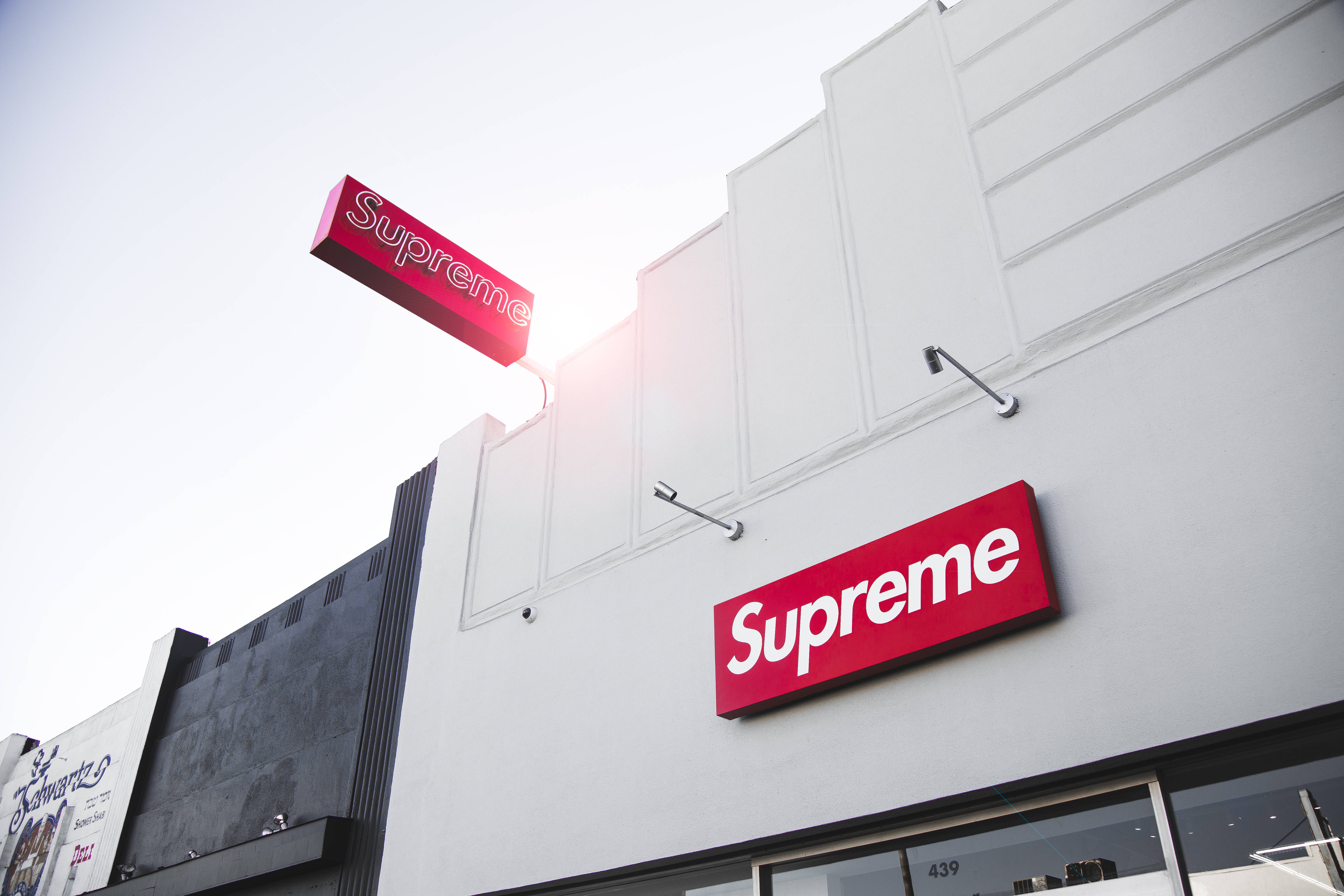 strange supreme 桌布 壁紙 — 晴朗天空下，低角度拍攝Supreme商店，鮮紅色標誌襯托明亮白色建築外牆。