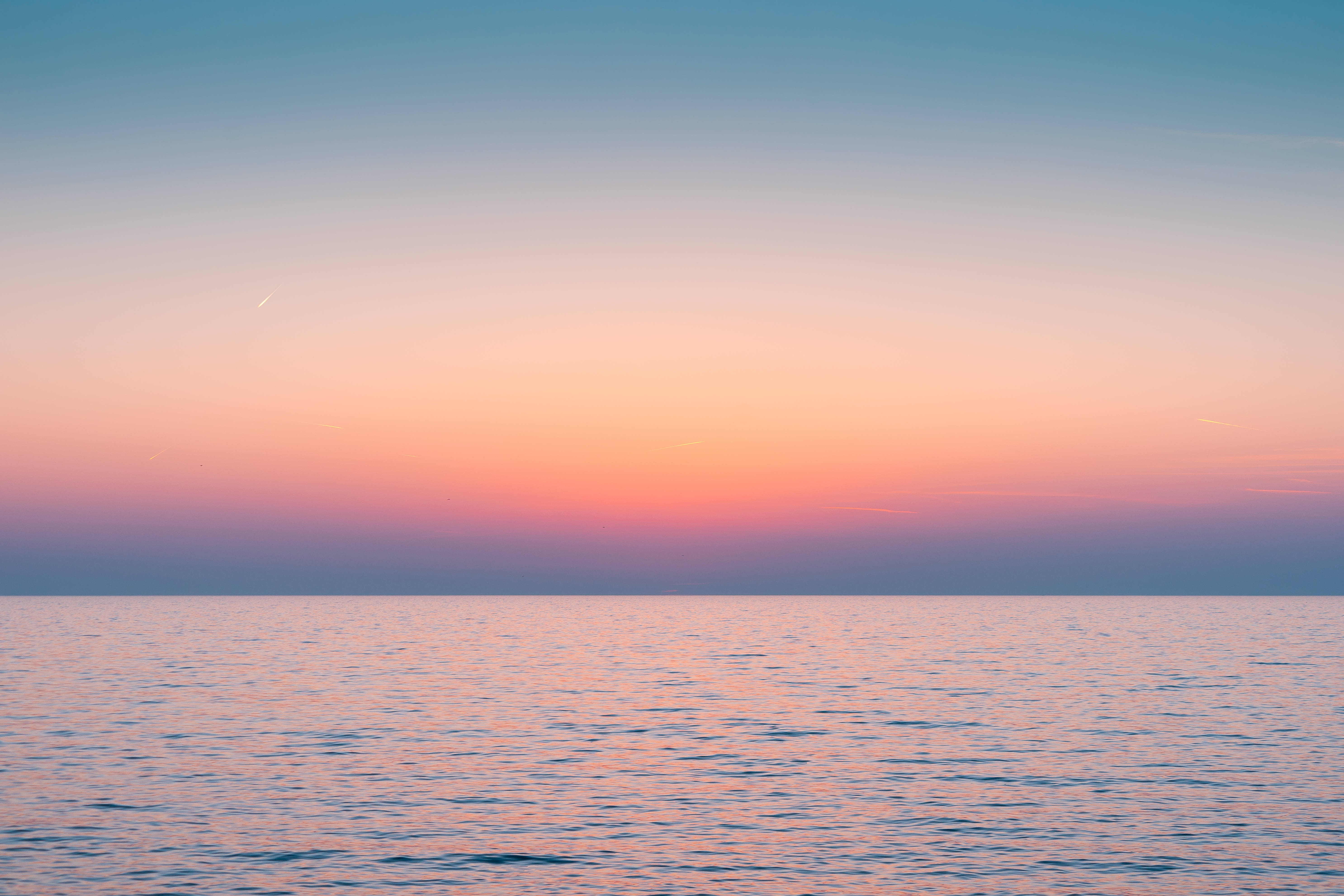 Aesthetic Sky 桌布 壁紙 — 晴朗天空下，平靜海洋在日落時分映照出柔和粉紅、橙和藍色調。