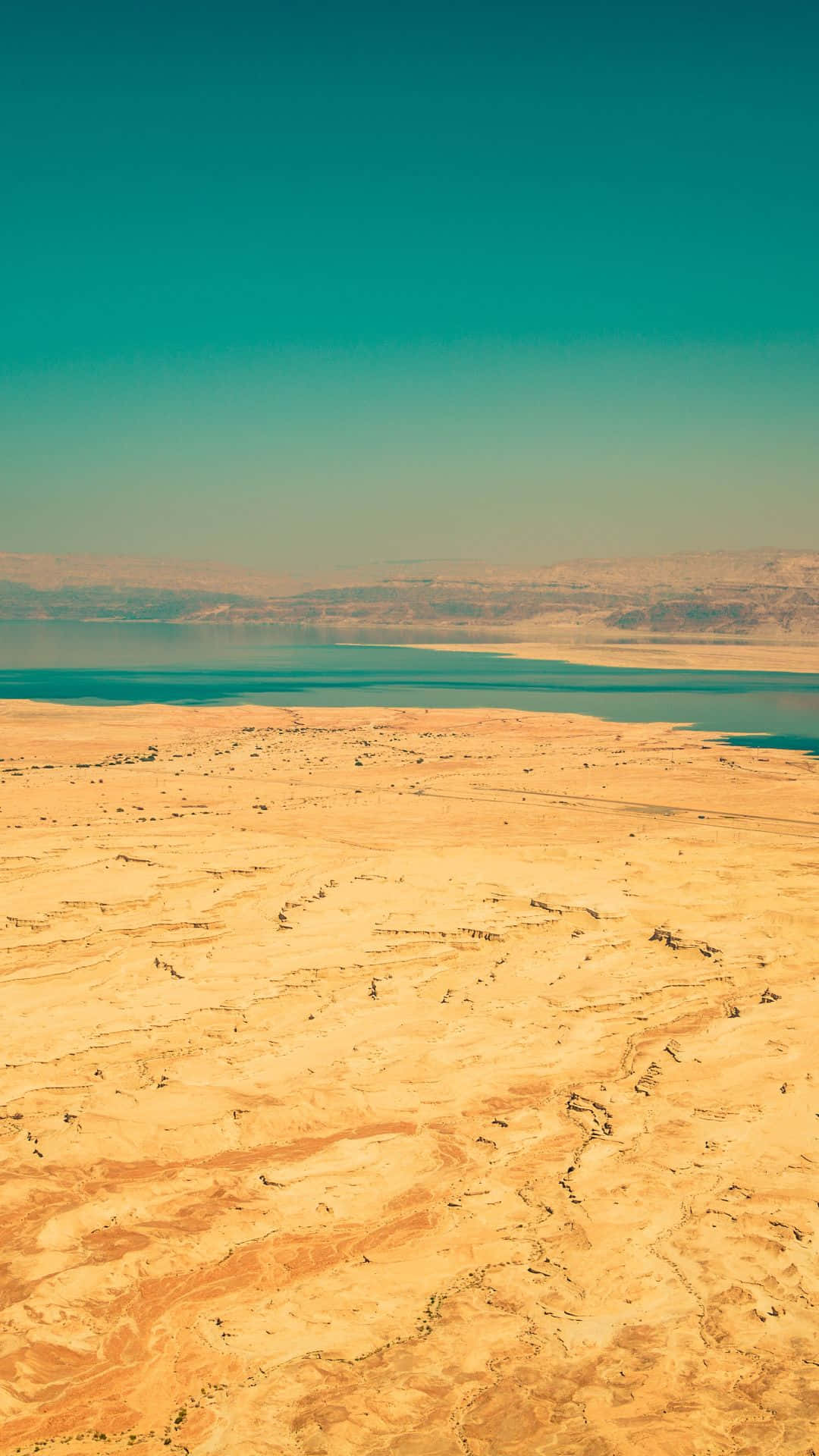 Israel 桌布 壁紙 — 晴朗天空下，廣闊沙漠中乾旱山丘之間鑲嵌著一個碧綠湖泊的航拍視圖。