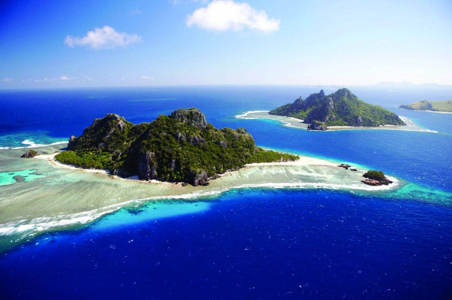 Fiji 桌布 壁紙 — 晴朗天空下，翠綠島嶼與白色沙灘被充滿活力的綠松石色和深藍色海水環繞的航拍視圖。