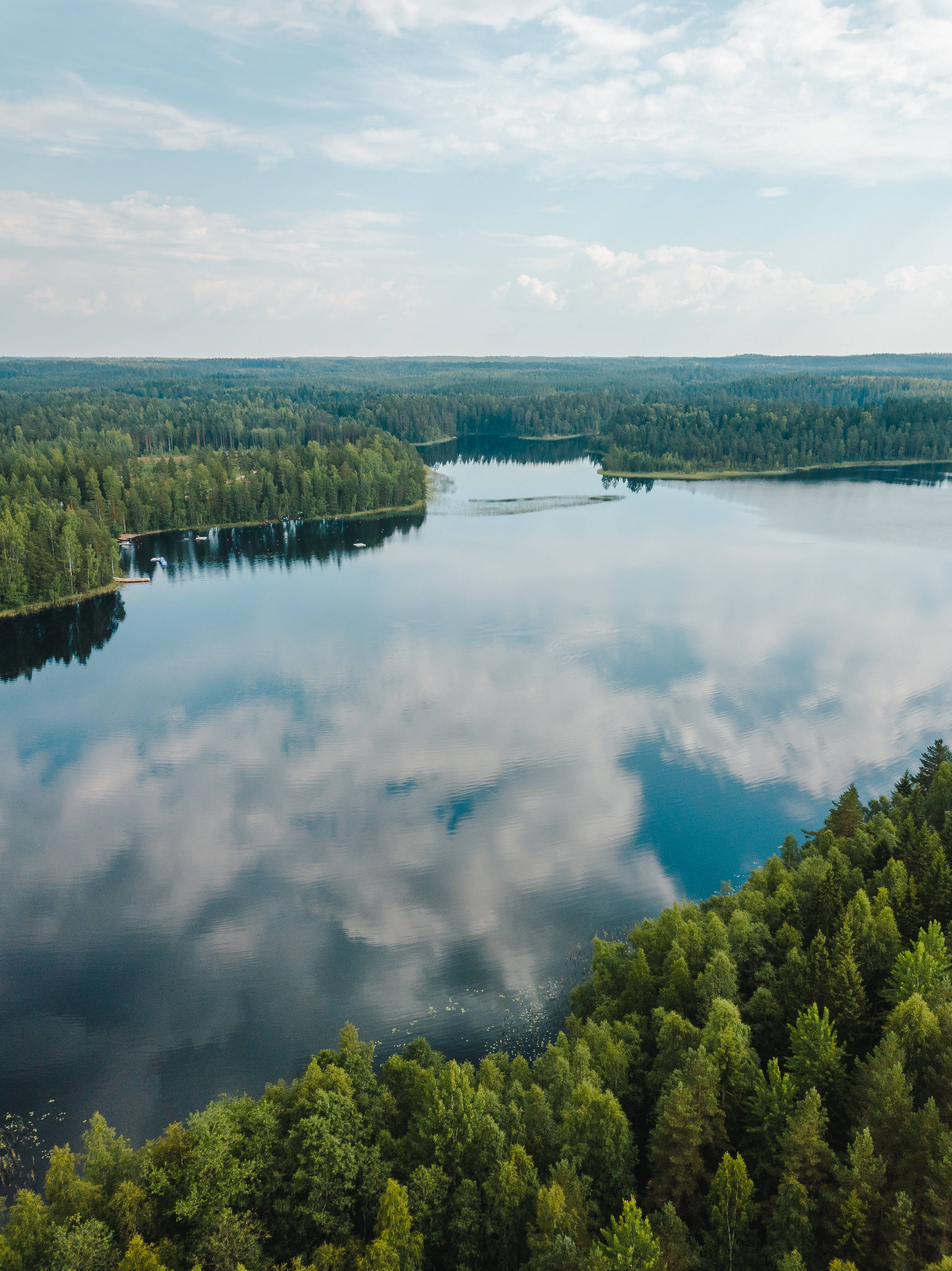 Finland 桌布 壁紙 — 晴朗天空下，茂密綠色森林環繞的寧靜湖泊倒映著蓬鬆雲朵的鳥瞰圖。