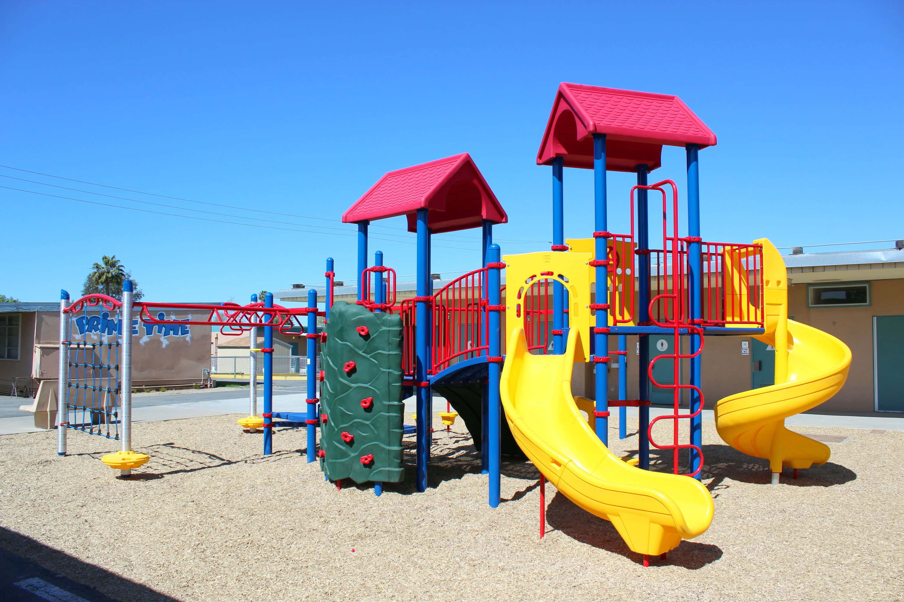 Playground 桌布 壁紙 — 晴朗日子裡，在清澈藍天下，充滿活力的遊樂場，有黃色溜滑梯、紅色屋頂和藍色結構。