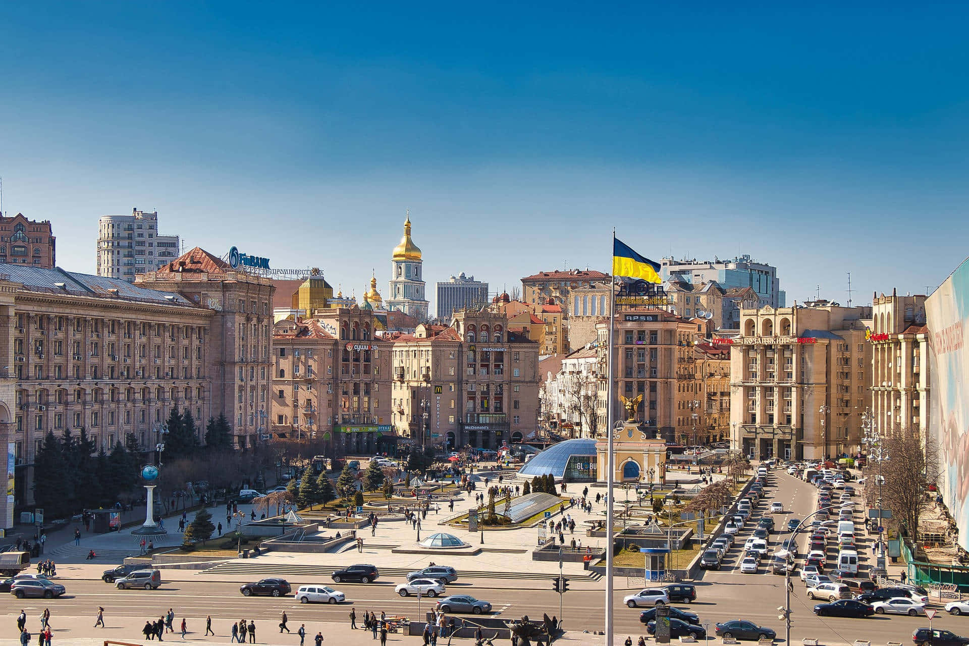 Ukraine 桌布 壁紙 — 晴朗明媚的一天，在一個繁忙的歐洲城市廣場，有歷史建築、金色圓頂和繁忙的交通，天空湛藍清澈。