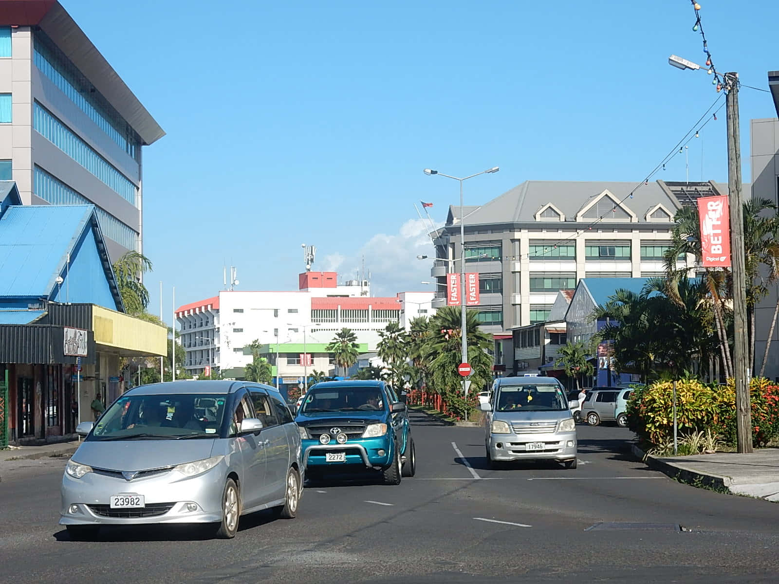 Road 桌布 壁紙 — 晴朗明媚的一天，在熱帶城市街道上，汽車駛過現代建築和棕櫚樹。
