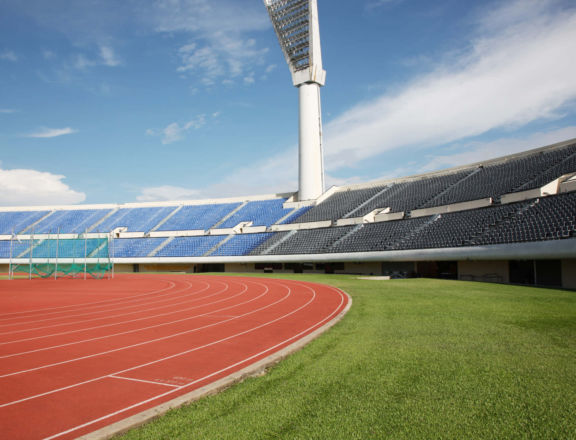 Stadium 桌布 壁紙 — 晴朗明媚的一天，空無一人的戶外體育場，紅色跑道和藍色座位，在清澈的藍天下。