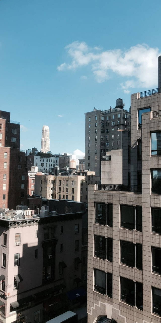 New York 桌布 壁紙 — 晴朗的藍天中飄著蓬鬆的白雲，俯瞰著密集的城市天際線，各式高樓大廈在清晰日光下矗立。