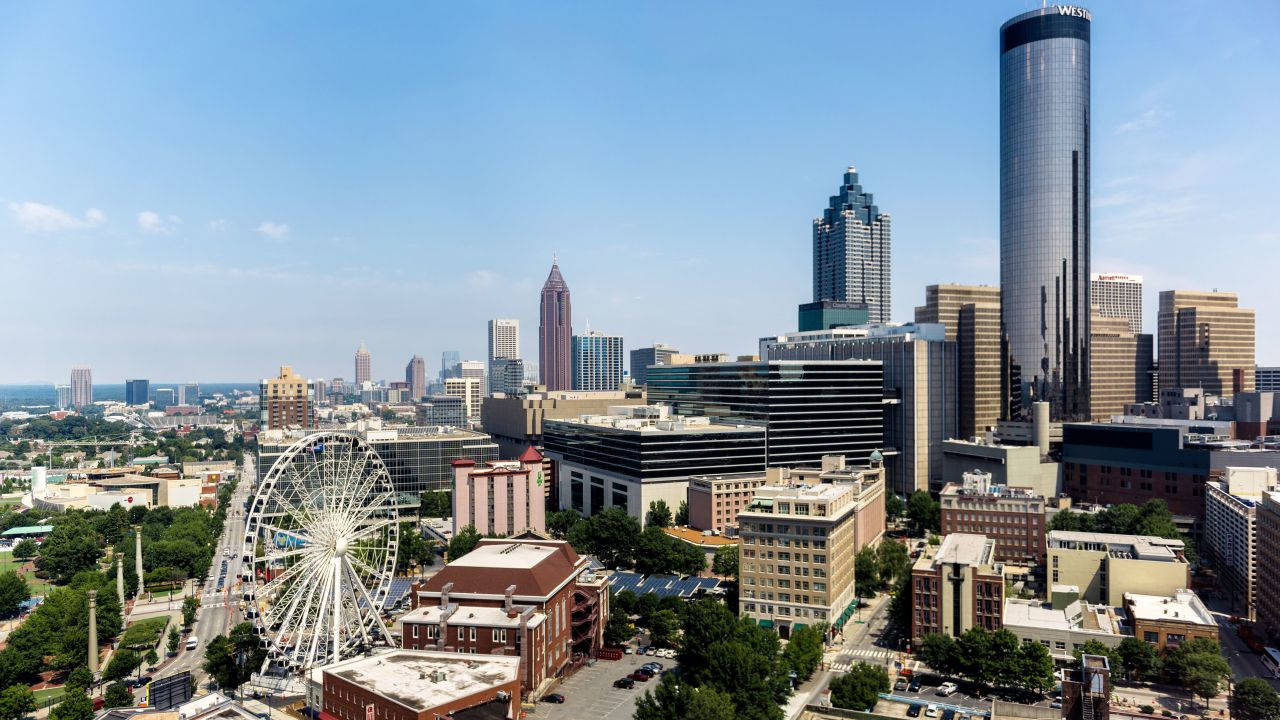 Atlanta 桌布 壁紙 — 晴朗藍天下，一個充滿活力的城市景觀鳥瞰圖，包含一個巨大的白色摩天輪和現代摩天大樓。