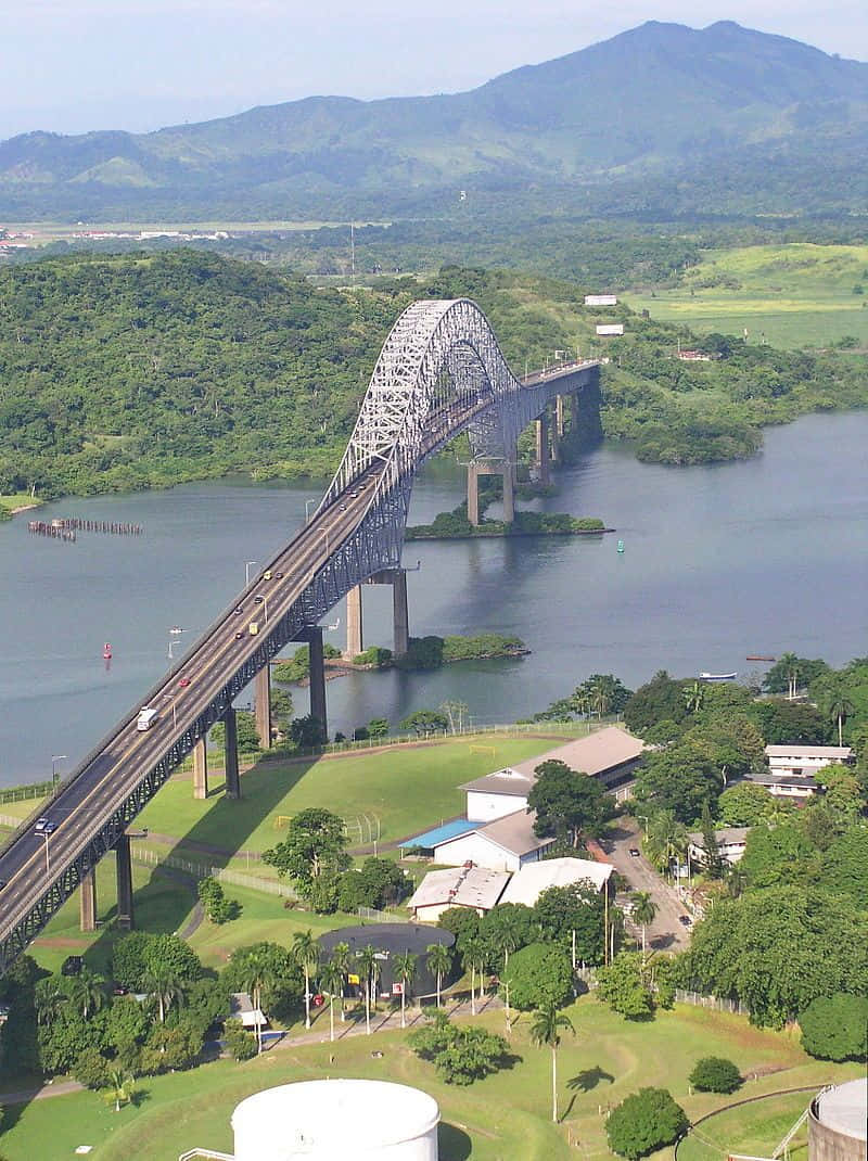 bridge 桌布 壁紙 — 晴朗藍天下，一座鋼拱橋橫跨寬闊河流，背景是鬱鬱蔥蔥的綠色山丘和山脈的鳥瞰圖。