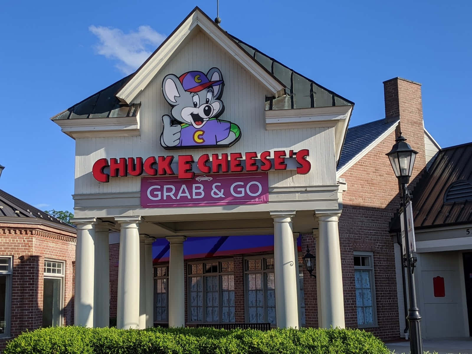 查克芝士 桌布 壁紙 — 晴朗藍天下，一間明亮的Chuck E Cheese's餐廳，卡通老鼠吉祥物豎起大拇指。