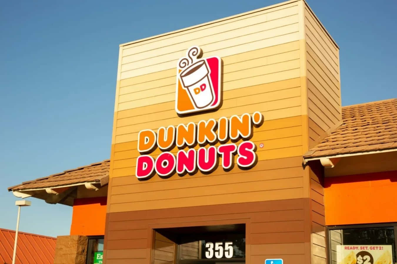 Dunkin Donuts 桌布 壁紙 — 晴朗藍天下，明亮的橙色Dunkin' Donuts店面，配以醒目的招牌和溫暖的陽光。