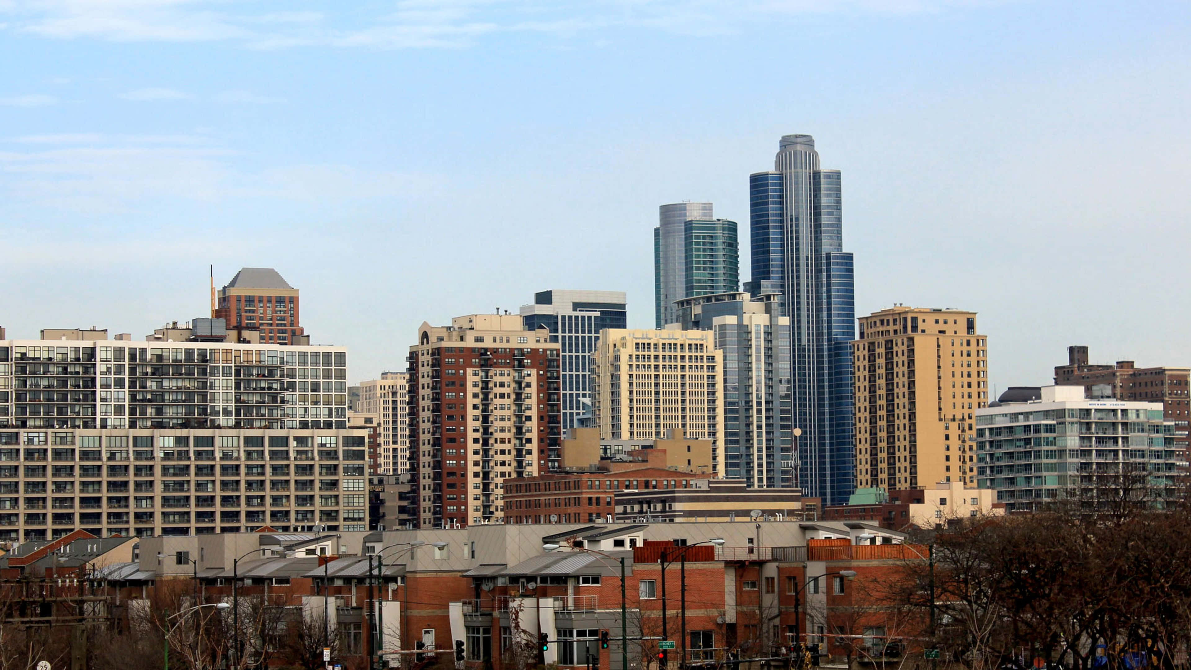 4K Ultra HD Chicago 桌布 壁紙 — 晴朗藍天下，現代城市天際線的全景視圖，包含玻璃摩天大樓和磚砌建築。