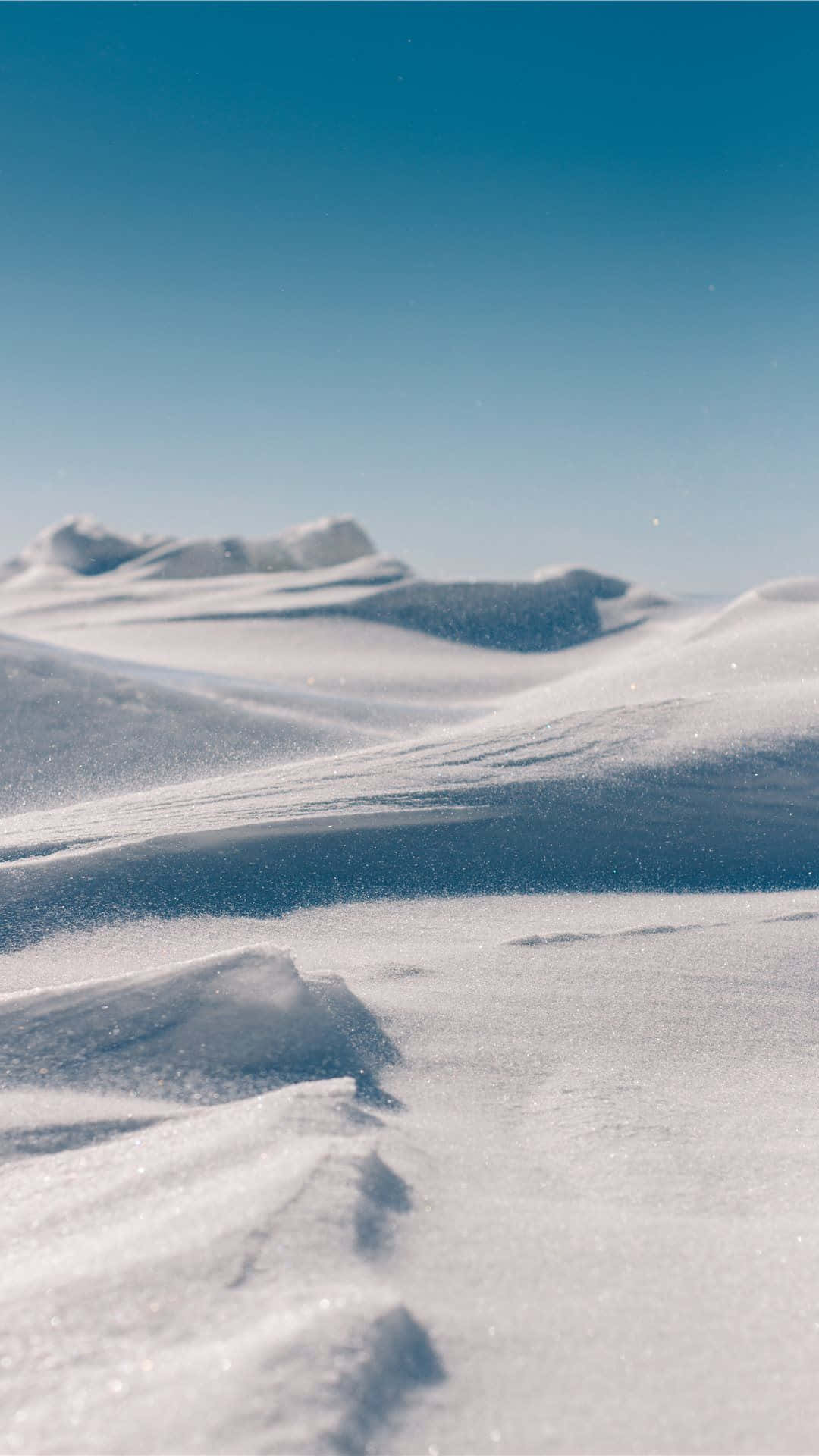 冬天 桌布 壁紙 — 晴朗藍天下，白雪覆蓋的沙丘和遠山構成的寧靜冬季景觀。