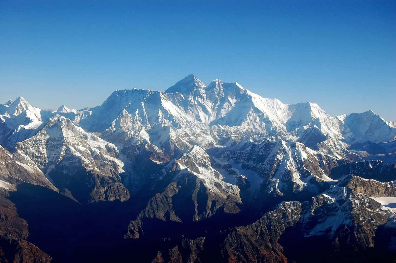 Mount Everest 桌布 壁紙 — 晴朗藍天下白雪覆蓋的喜馬拉雅山峰的航拍視角，崎嶇岩石斜坡處於陰影中。