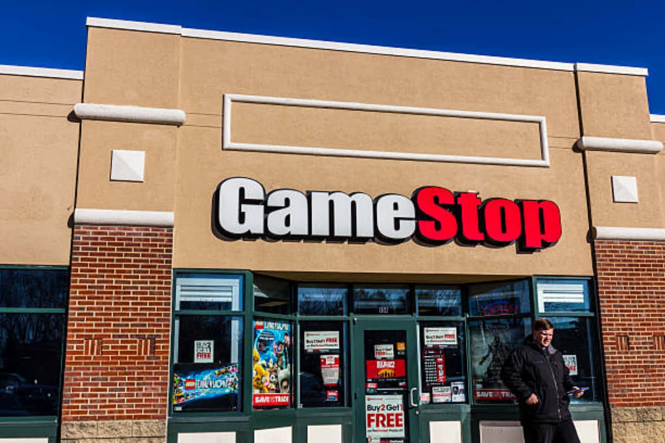 GameStop 桌布 壁紙 — 晴朗陽光普照的日子，在GameStop商店外，一名男子站在清澈的藍天下。