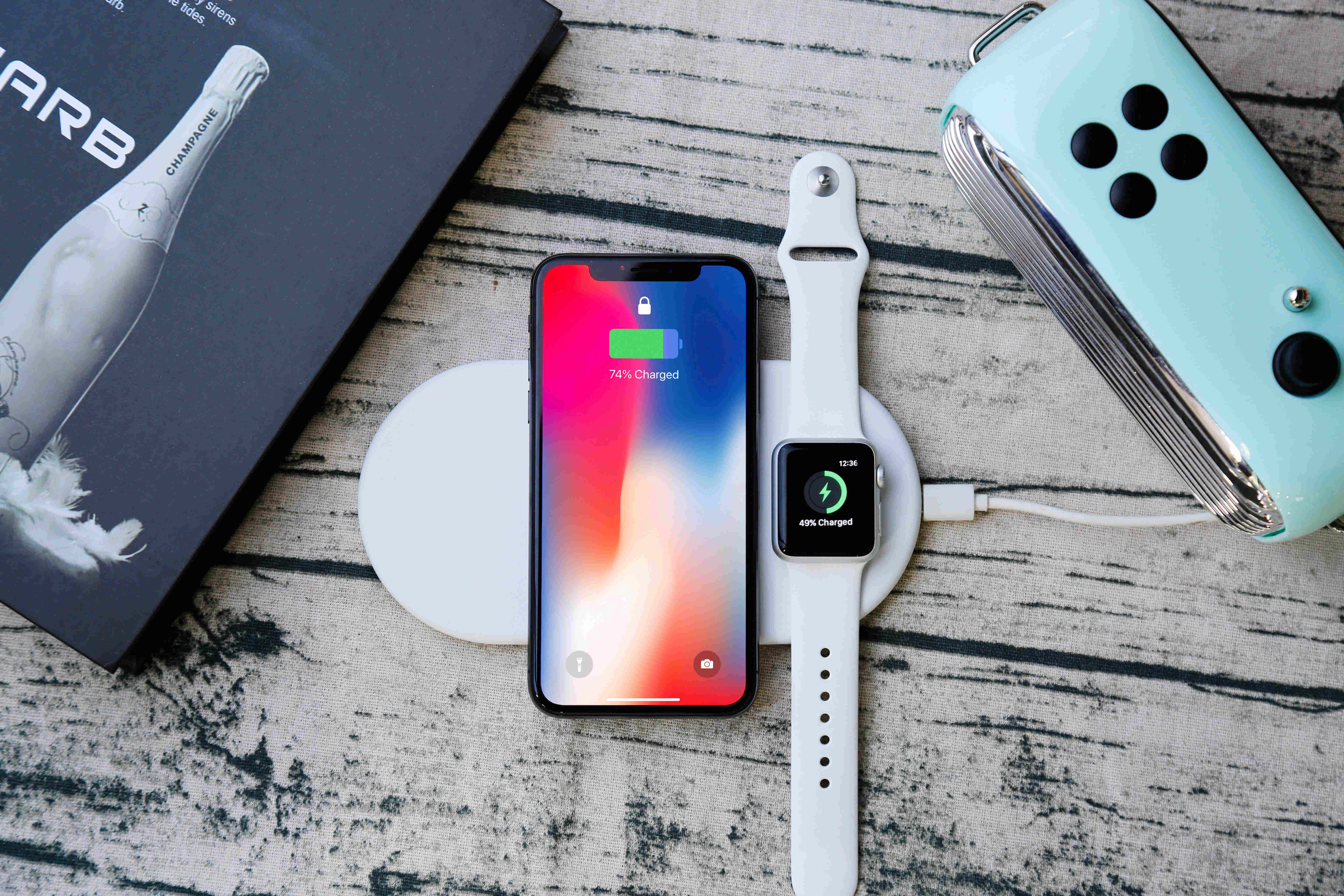 Wireless Charging 桌布 壁紙 — 智慧型手機和智慧手錶在白色充電板上無線充電，旁邊是薄荷色控制台和香檳書，置於風化木上。