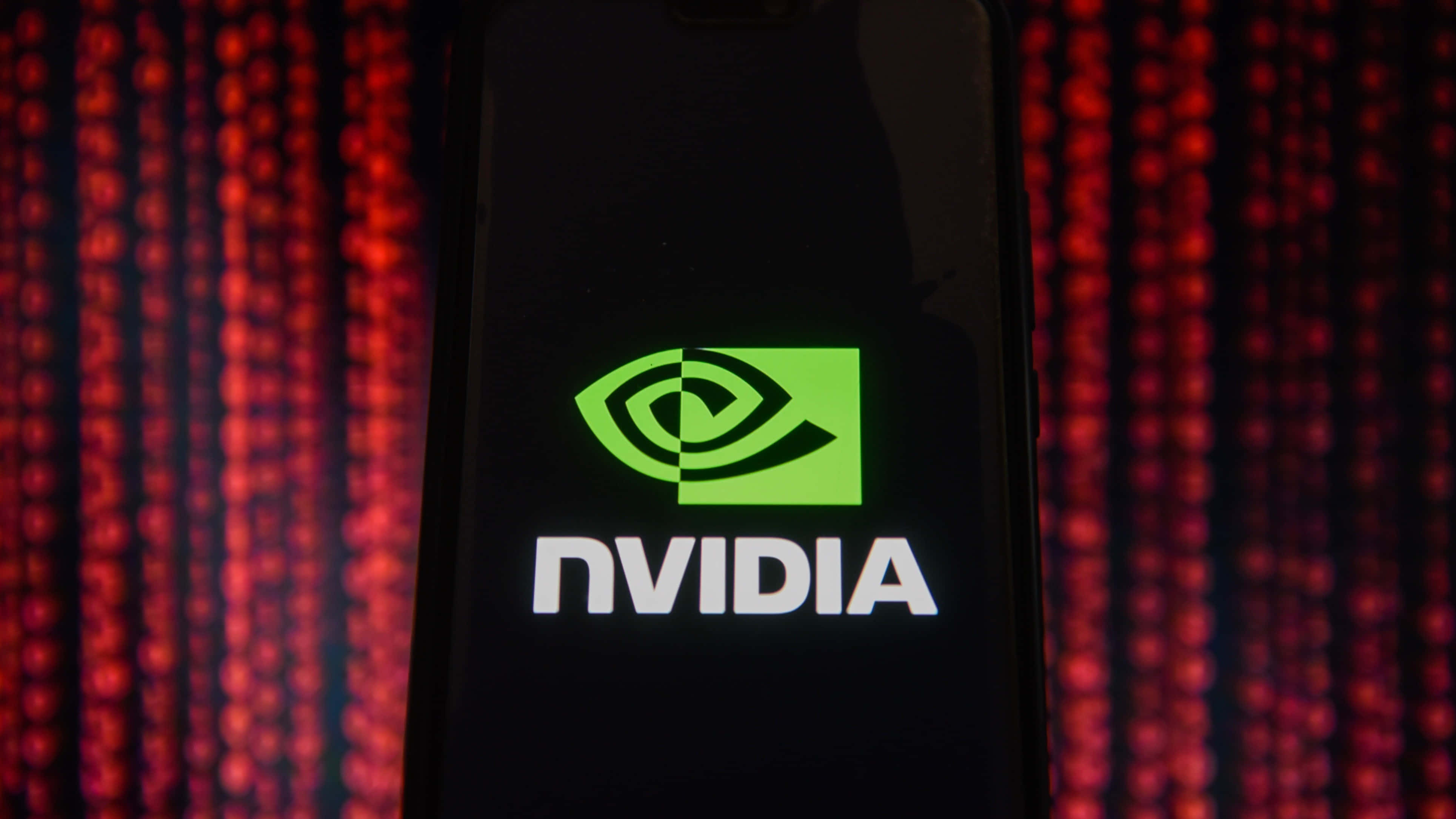 nvidia 桌布 壁紙 — 智慧型手機在紅色數位數據流背景下顯示發光的綠色NVIDIA標誌。