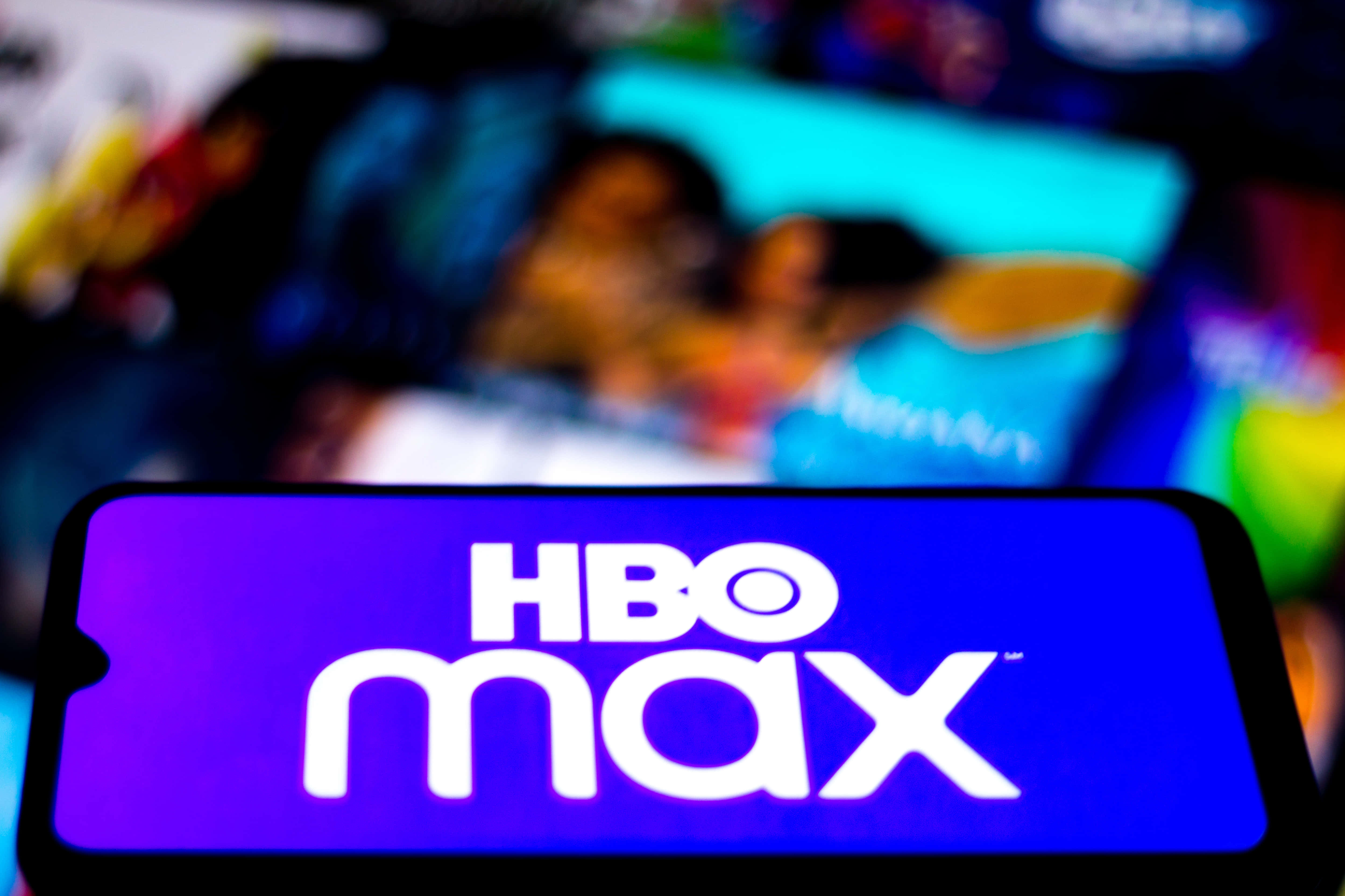HBO 桌布 壁紙 — 智慧型手機清晰顯示HBO Max標誌，背景是模糊的彩色串流服務縮圖。