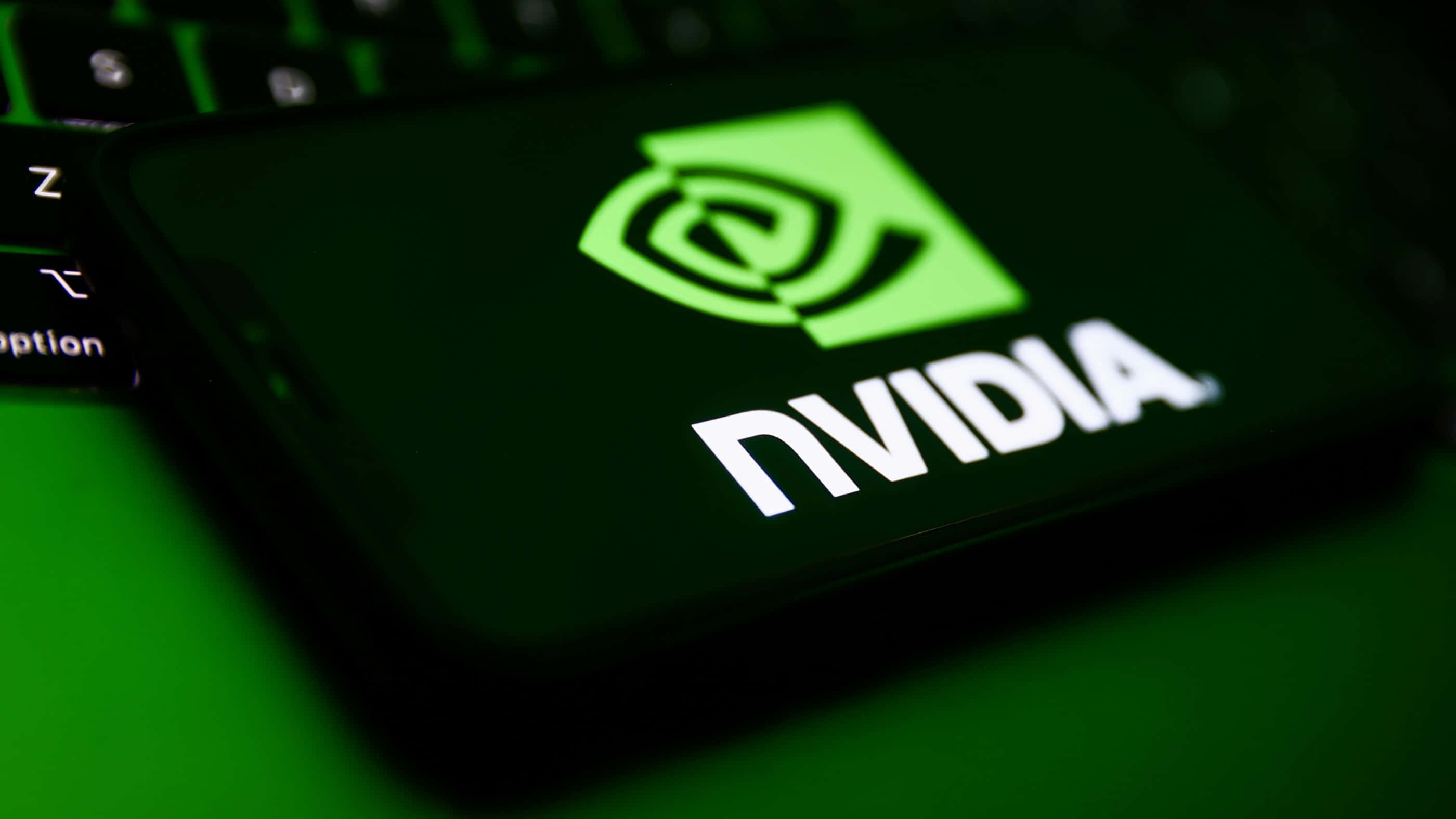 nvidia 桌布 壁紙 — 智慧型手機特寫，顯示發光的綠色NVIDIA標誌，放在深色鍵盤上。