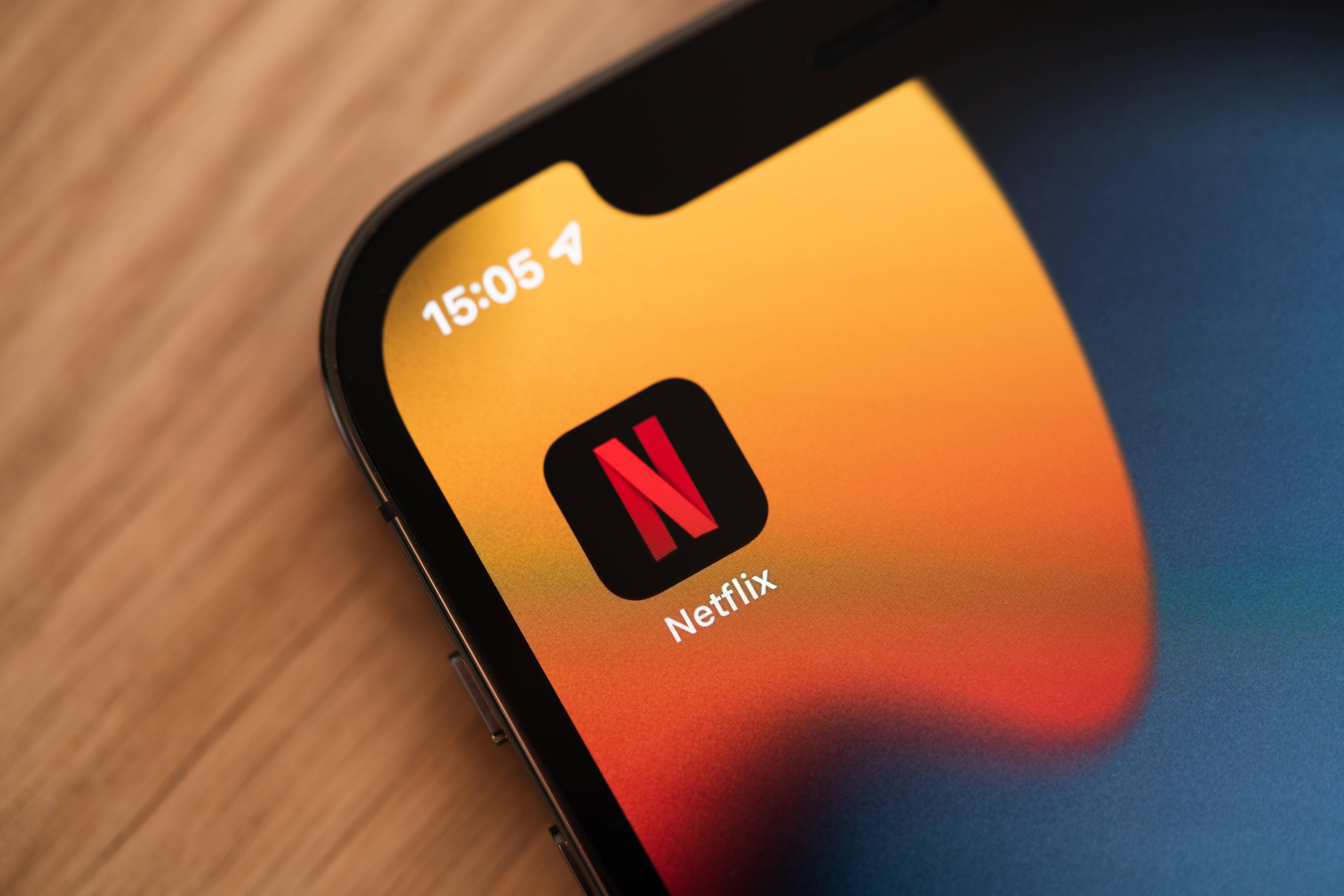 標誌 桌布 壁紙 — 智慧型手機的特寫，顯示Netflix應用程式圖示在充滿活力的漸變桌布上，放置在木質表面上。