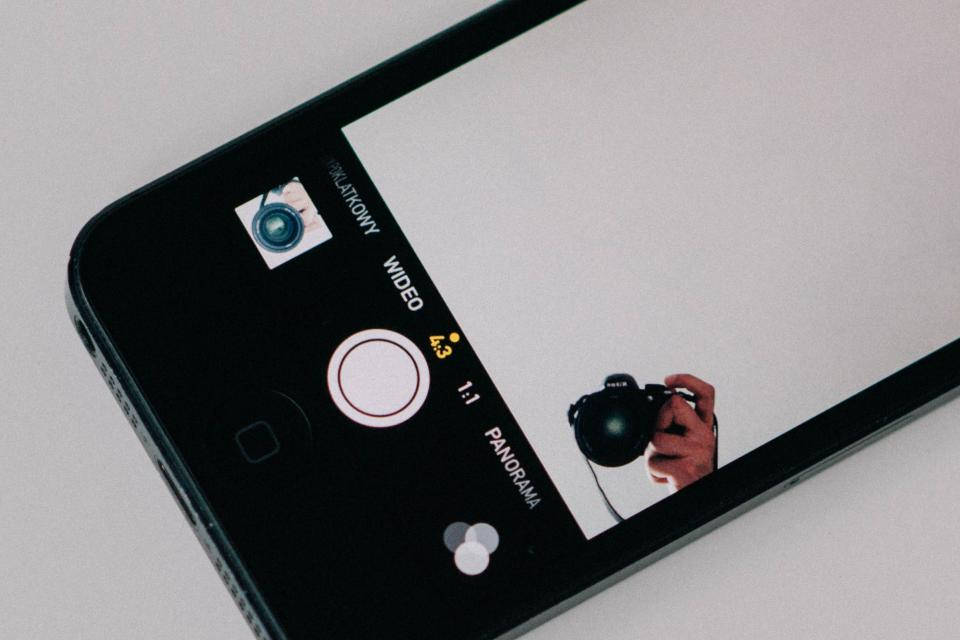 photography iPhone 桌布 壁紙 — 智慧型手機相機螢幕的特寫，顯示一隻手在即時取景中拿著 DSLR 相機。