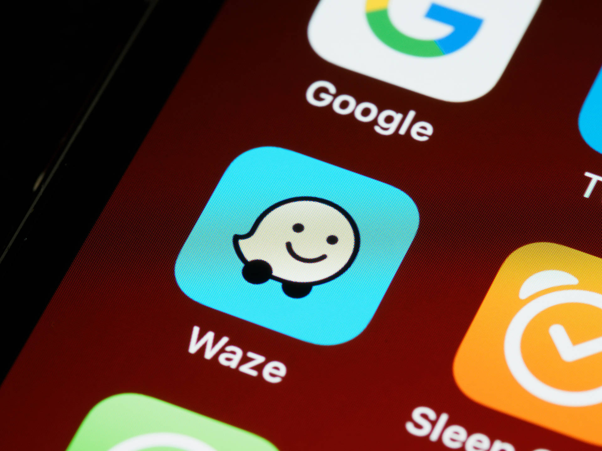 智慧型手機螢幕顯示Waze應用程式圖標，帶有微笑鬼魂吉祥物。 — iPhone 14 壁紙
