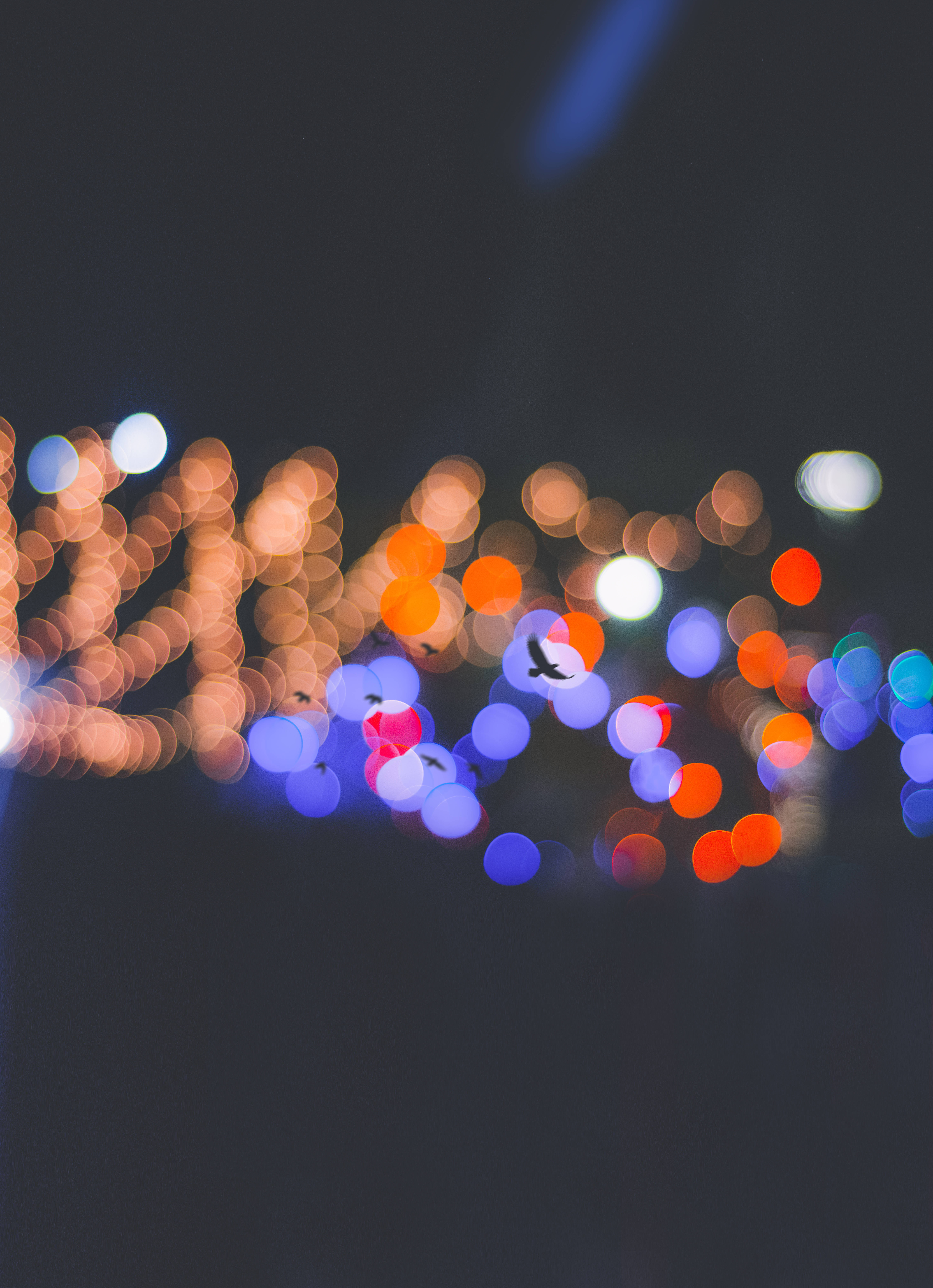 Bokeh 桌布 壁紙 — 暖橙色和冷藍色的散景燈光在黑暗的天空中模糊，剪影鳥兒飛過。