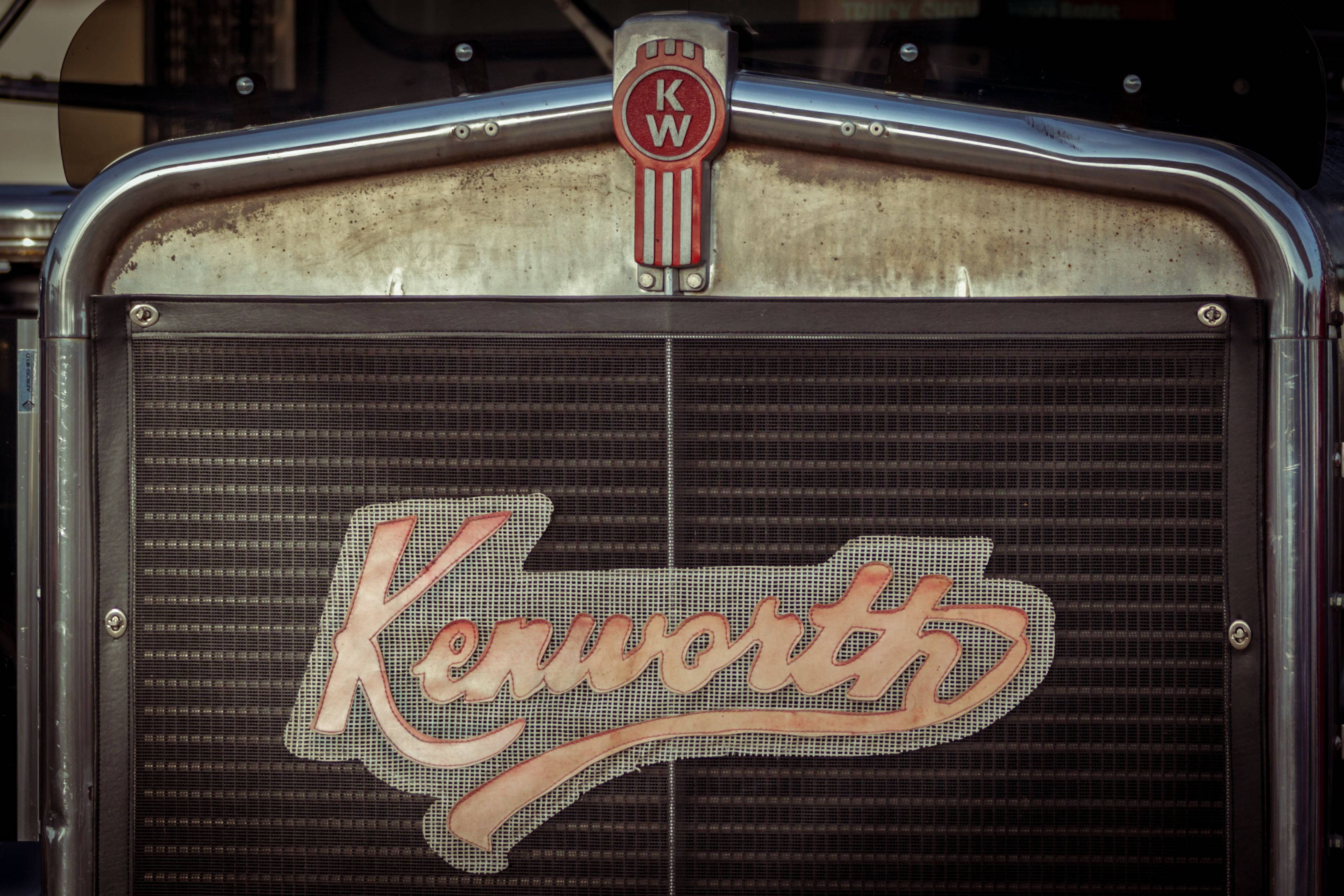 Kenworth 桌布 壁紙 — 暖色燈光下，經典Kenworth卡車格柵的特寫，帶有鍍鉻裝飾和褪色標誌。