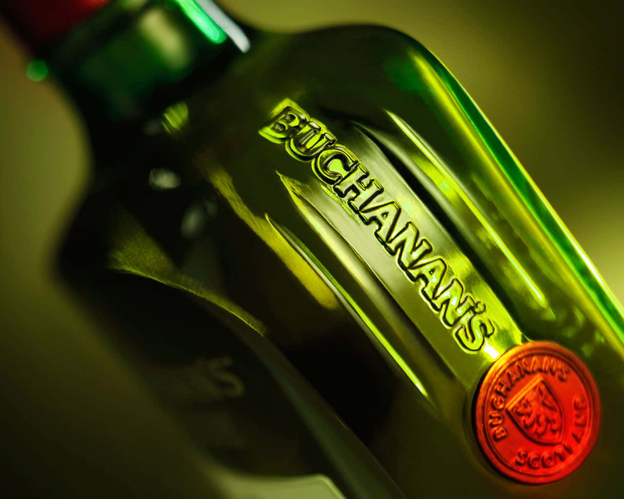 booze 桌布 壁紙 — 暖色燈光下，綠色Buchanan's威士忌酒瓶的特寫，帶有發光的紅色封條。
