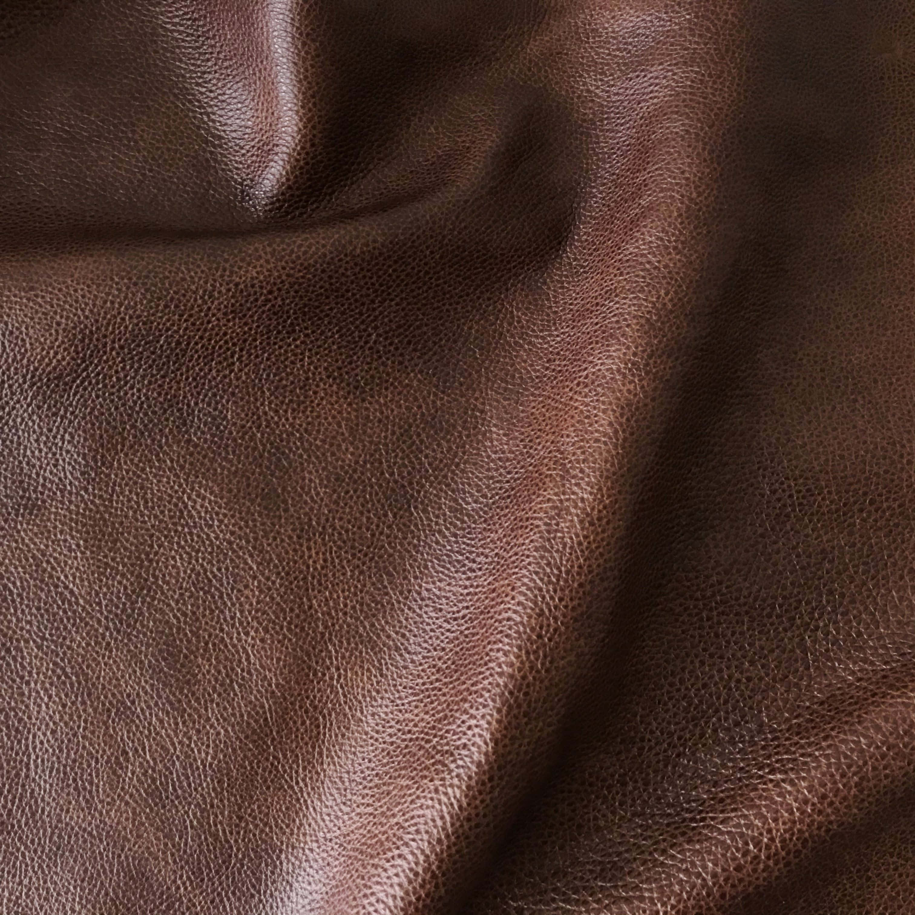 texture 桌布 壁紙 — 暖色燈光下，豐富棕色皮革的特寫，展現天然粒面紋理與柔軟皺褶。