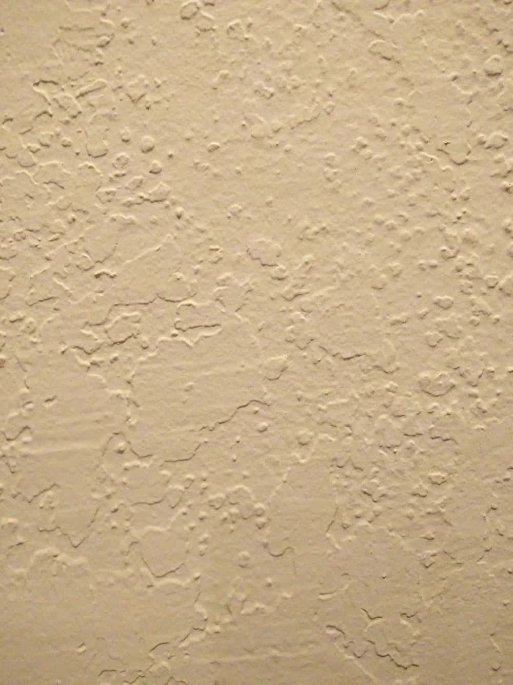 wall 桌布 壁紙 — 暖色燈光下米色灰泥牆的特寫，帶有紋理凸起和裂縫。