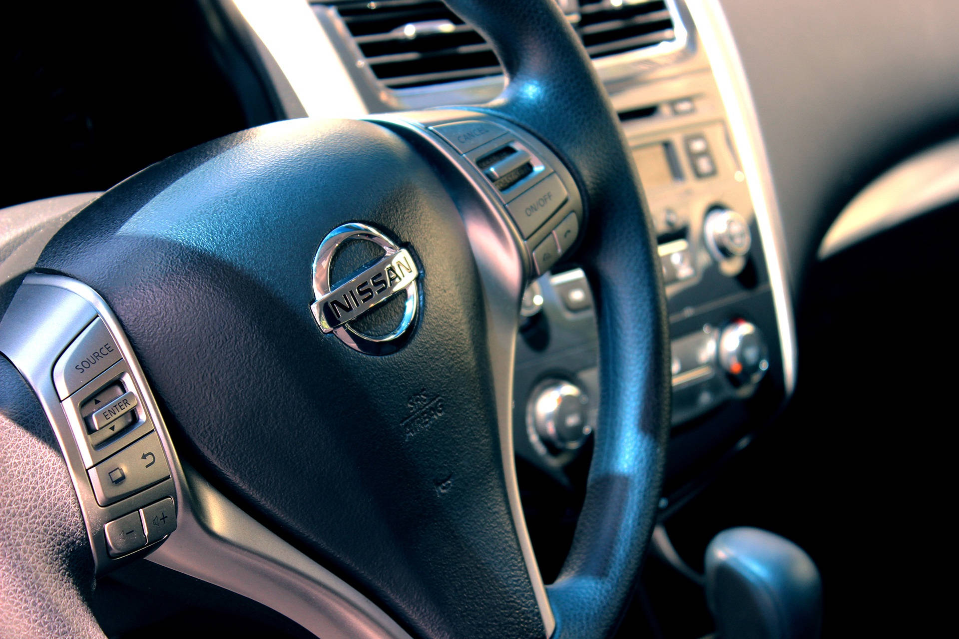 Nissan 桌布 壁紙 — 暖色燈光下黑色皮革日產方向盤特寫，帶有銀色控制鍵和儀表板細節。
