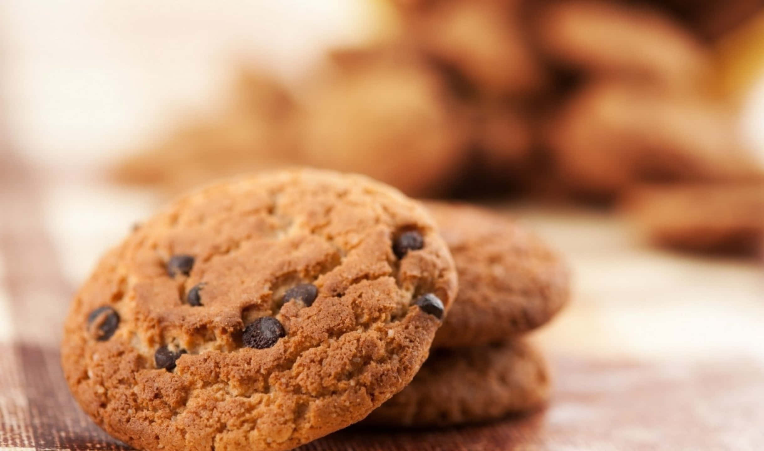 Cookies 桌布 壁紙 — 暖金色巧克力餅乾誘人地堆疊在木質表面上，背景餅乾模糊的特寫。