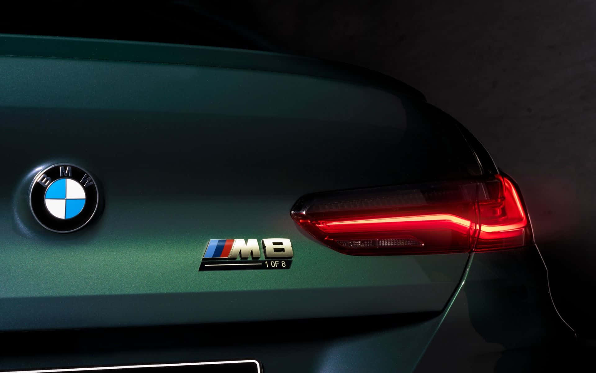 Bmw Cars 桌布 壁紙 — 暗綠色BMW M8在昏暗燈光下發光的紅色尾燈和「1 of 8」徽章的近距離特寫。