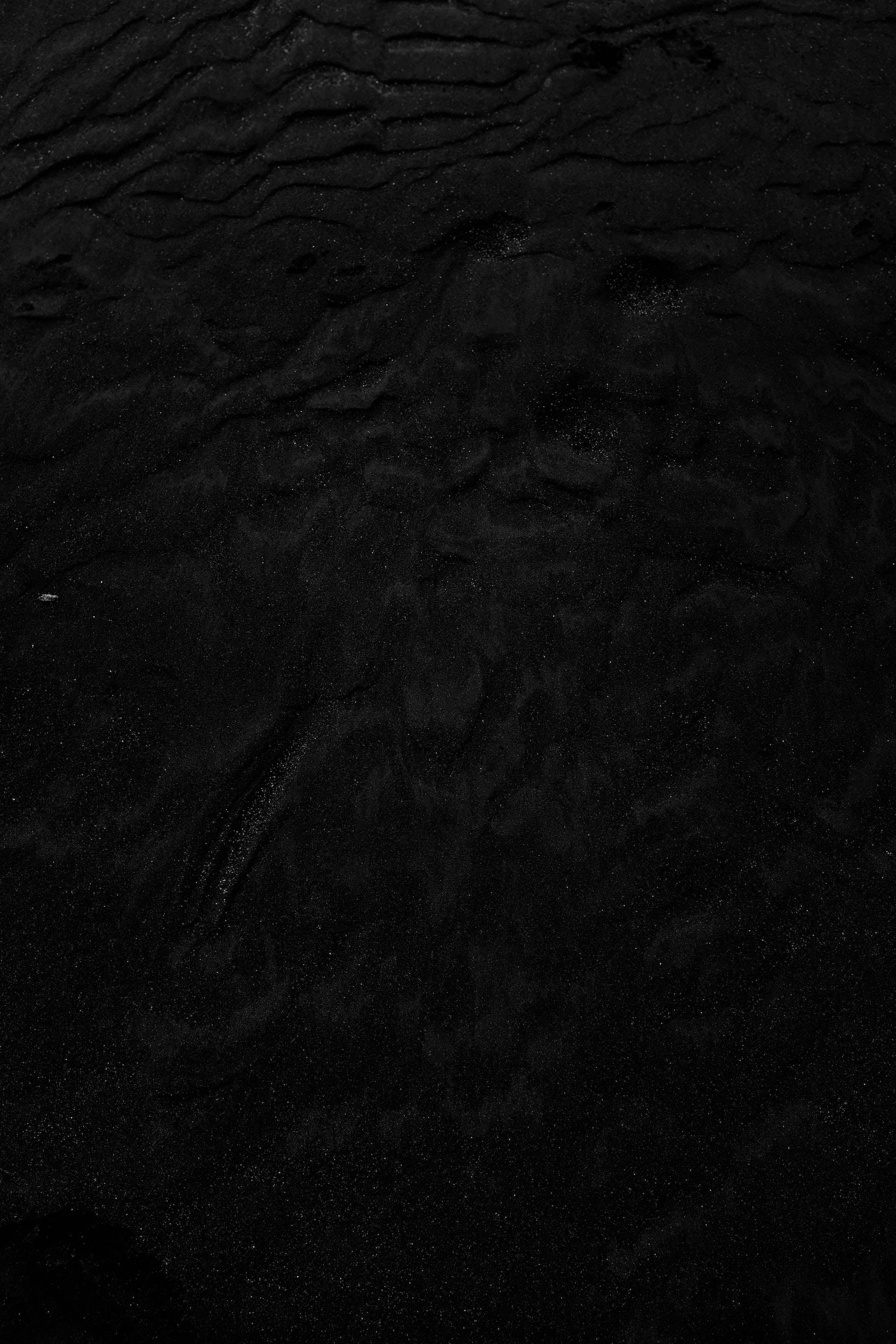 black aesthetic tumblr iPhone 桌布 壁紙 — 暗色紋理沙粒的微距特寫，帶有細微波紋和散落的小斑點，處於昏暗光線下。
