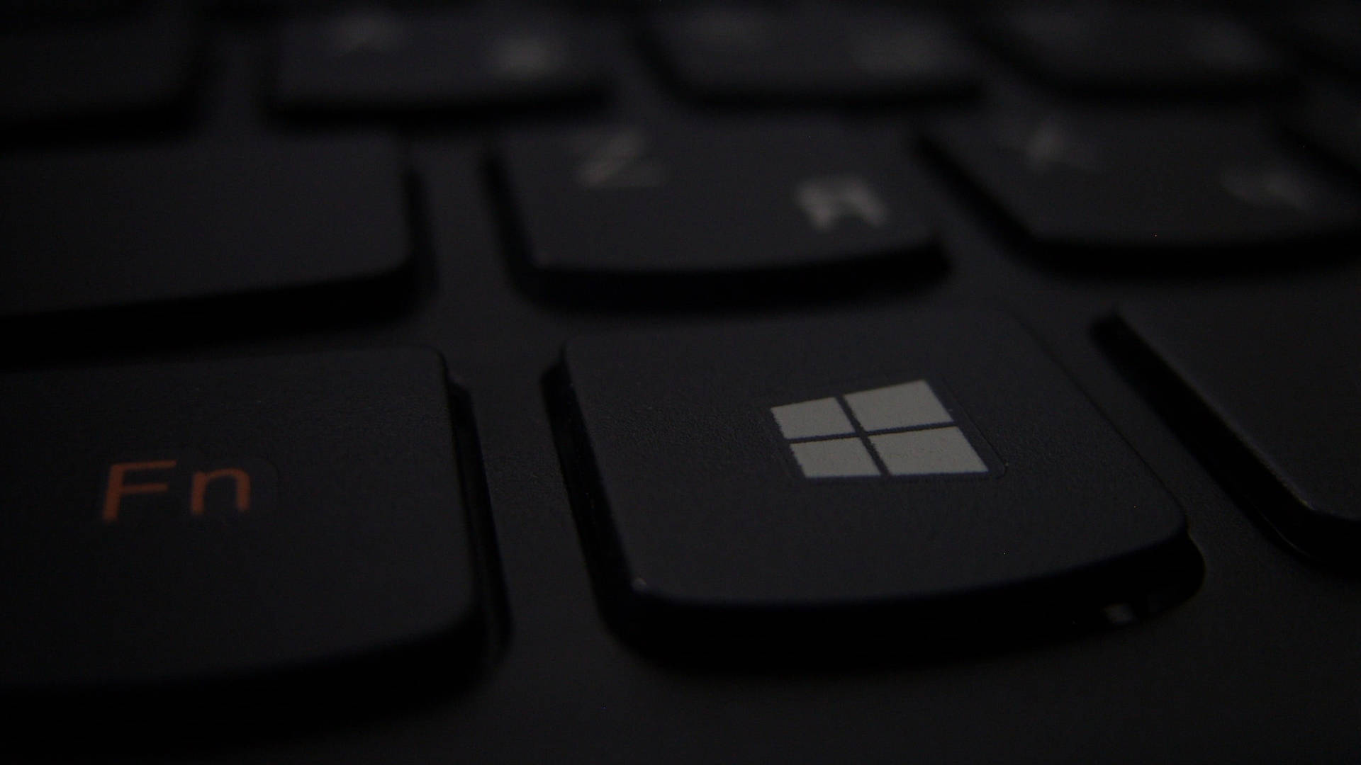 黑色鍵盤的特寫，帶有發光橙色 Fn 鍵和亮起的 Windows 標誌鍵。 — 4K筆電壁紙 壁紙