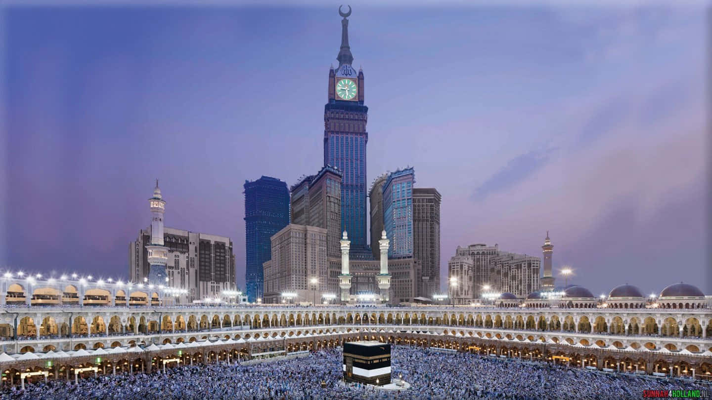 Makkah 桌布 壁紙 — 暮色中，人群聚集在卡巴天房周圍，麥加大清真寺後方聳立著燈火通明的摩天大樓。