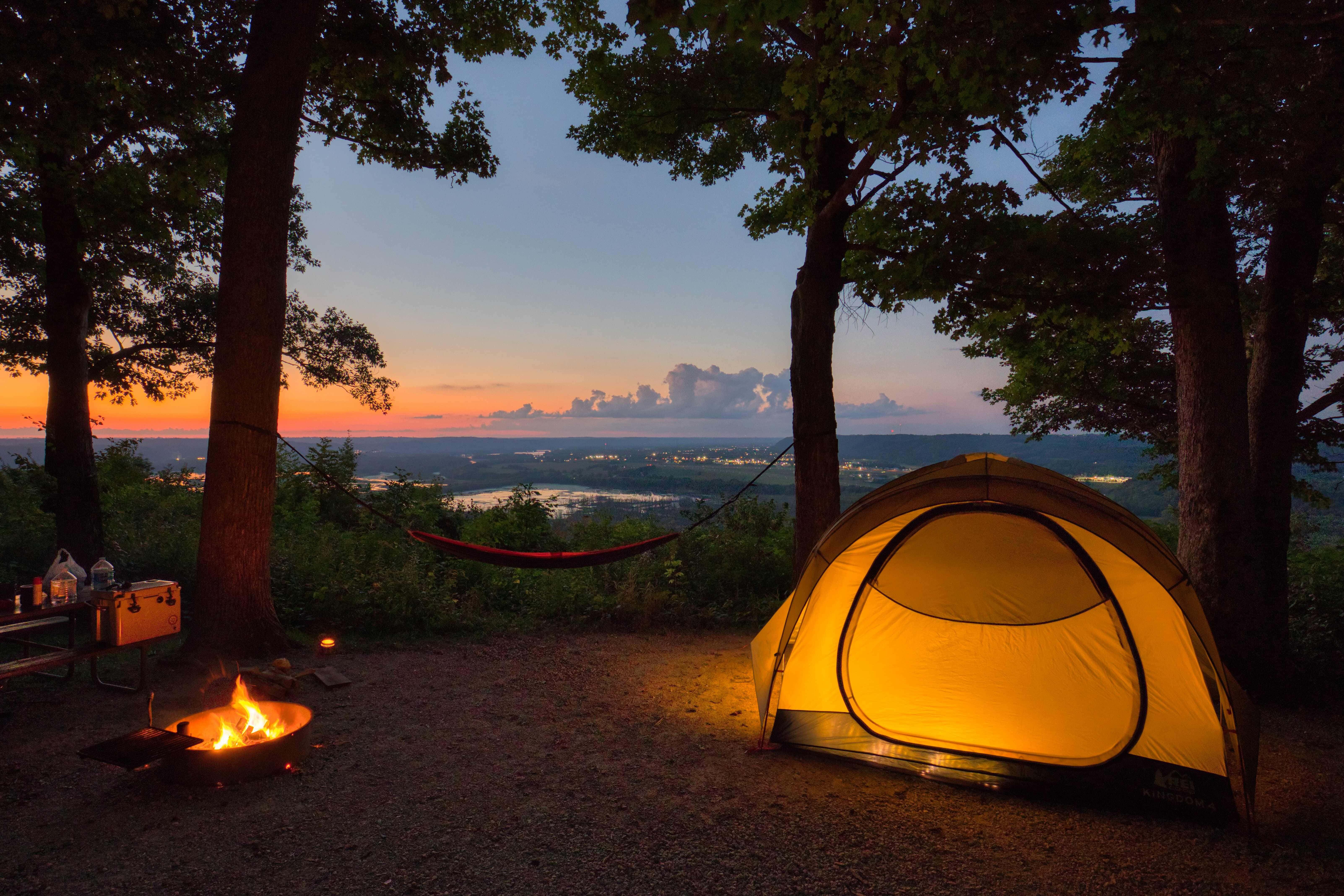 Camping 桌布 壁紙 — 暮色中，樹林間閃爍的帳篷和營火，俯瞰著遠方燈火點點的山谷。