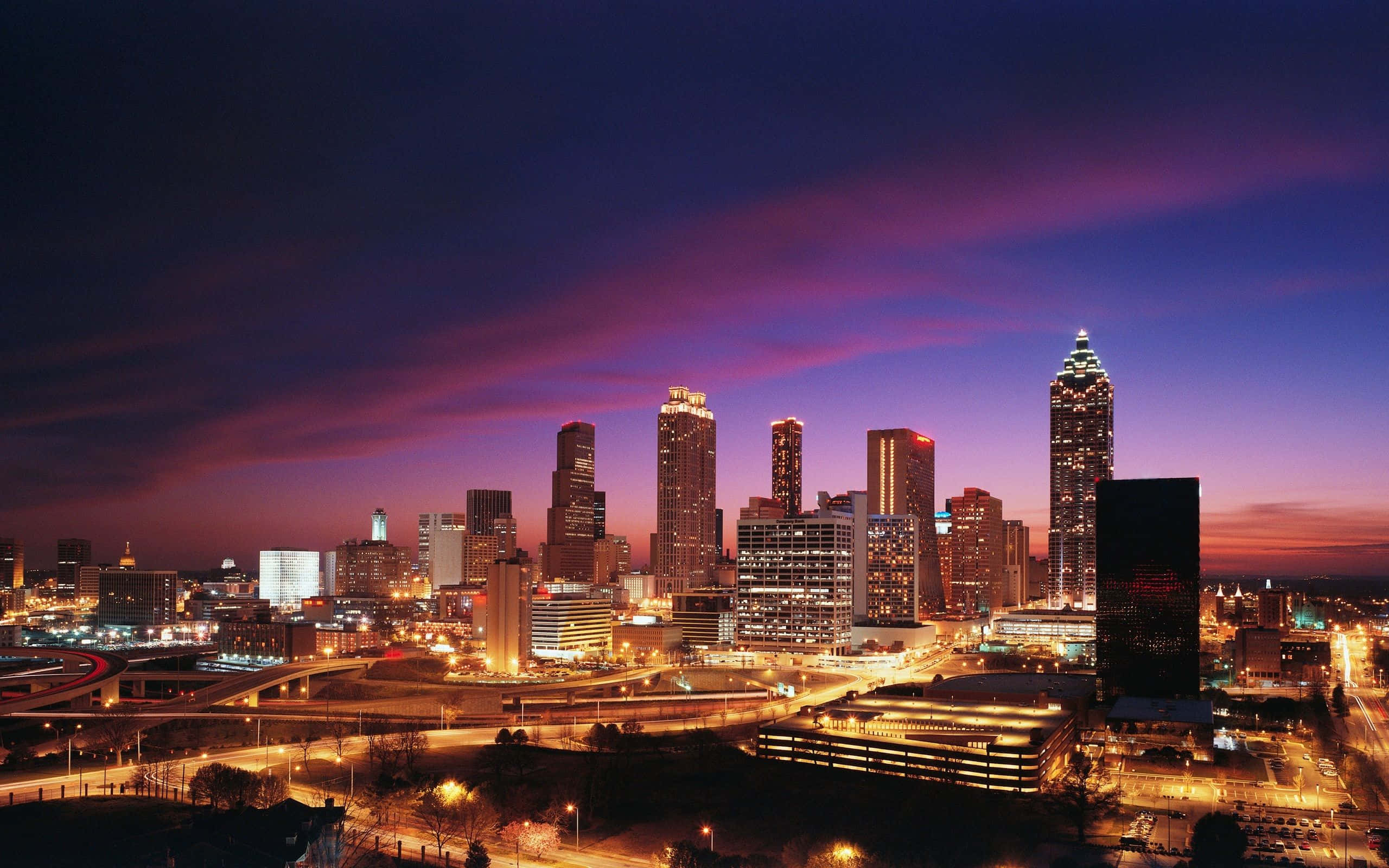 Atlanta Georgia 桌布 壁紙 — 暮色中充滿活力的城市天際線，紫色和橙色的天空映照著發光的摩天大樓和明亮的道路。