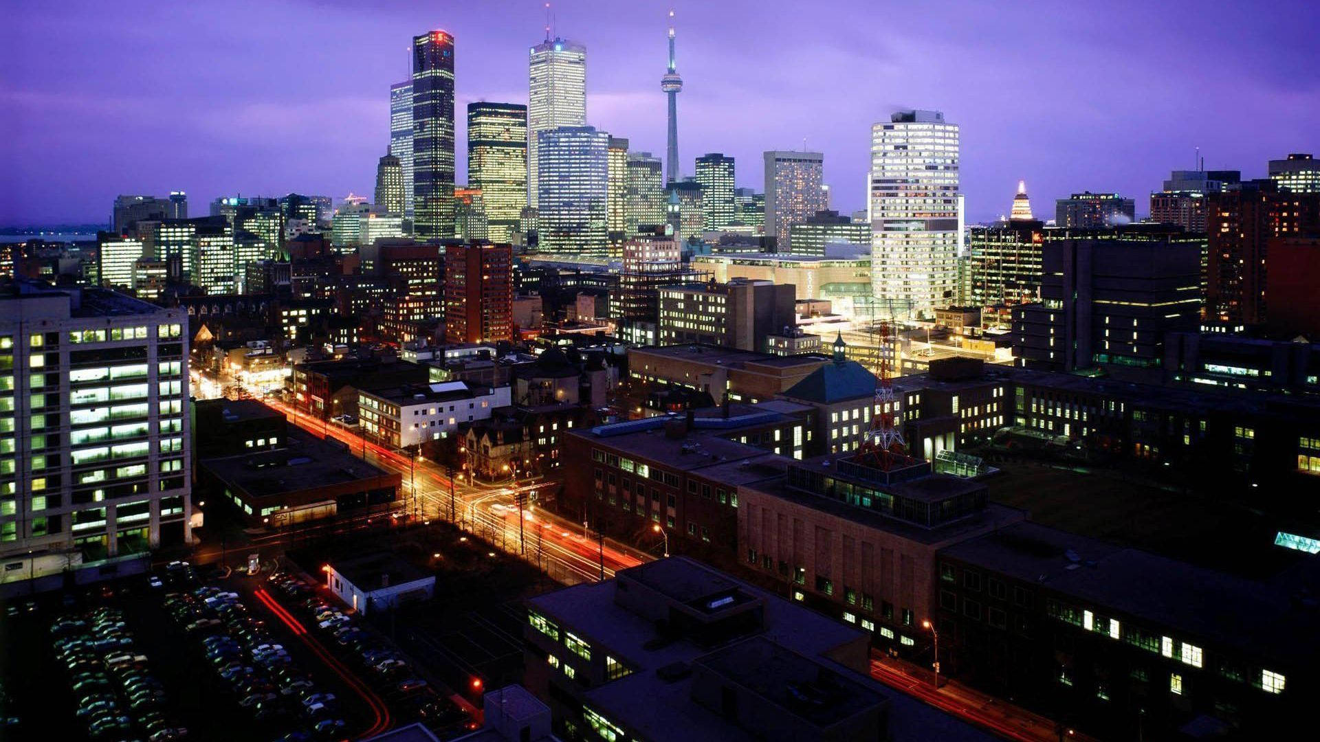 Ontario 桌布 壁紙 — 暮色中充滿活力的城市景觀，發光的摩天大樓和流動的交通燈光映襯著紫色的天空。