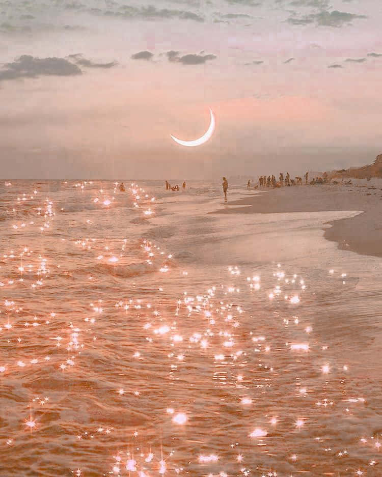 Peachy Aesthetic 桌布 壁紙 — 暮色中寧靜的海灘，閃爍的粉紅色海水上方懸掛著發光的彎月，海岸邊有剪影般的人影。