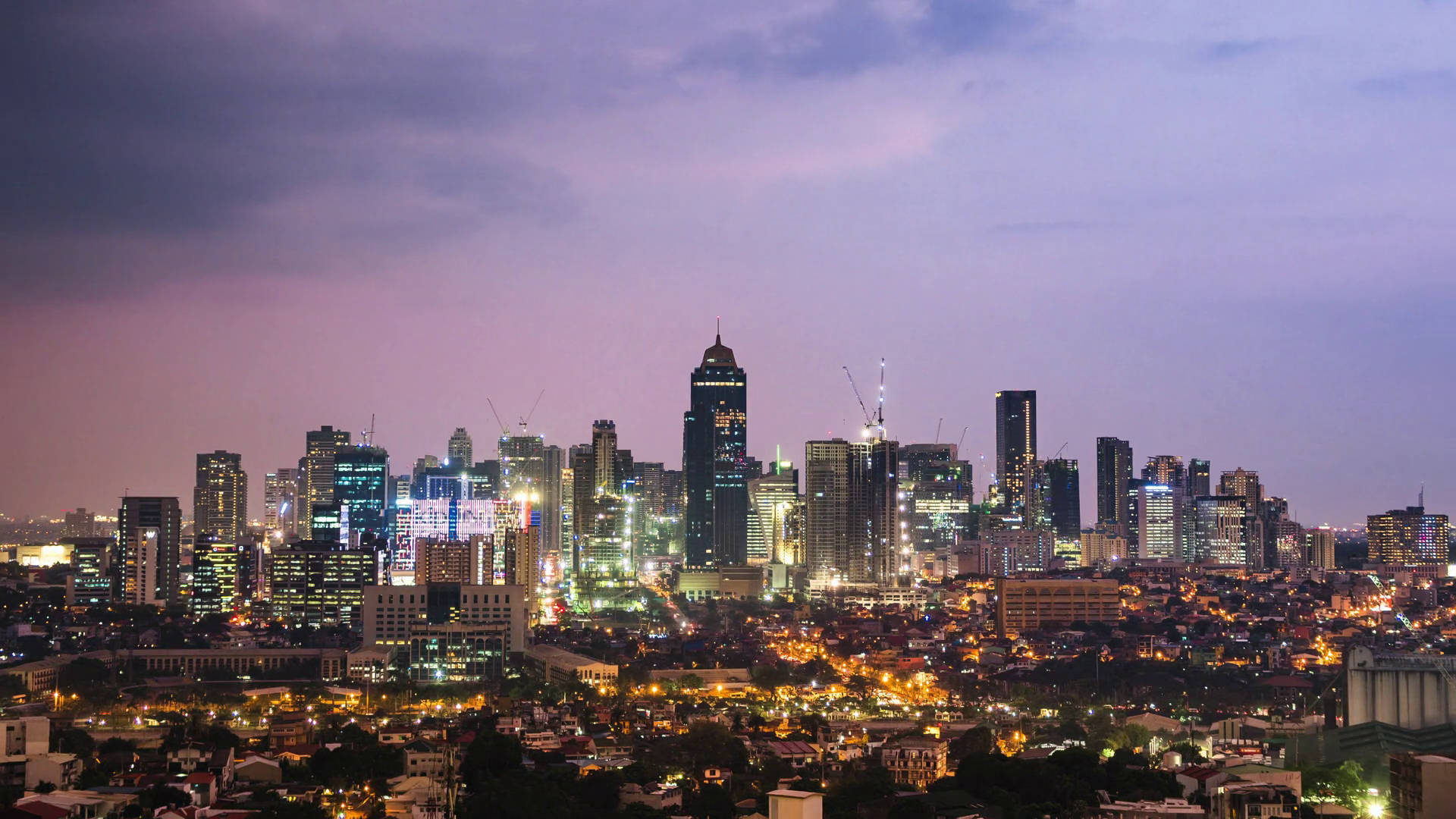 Manila 桌布 壁紙 — 暮色中廣闊的城市天際線，閃爍的摩天大樓和溫暖的路燈映襯著紫色的天空。