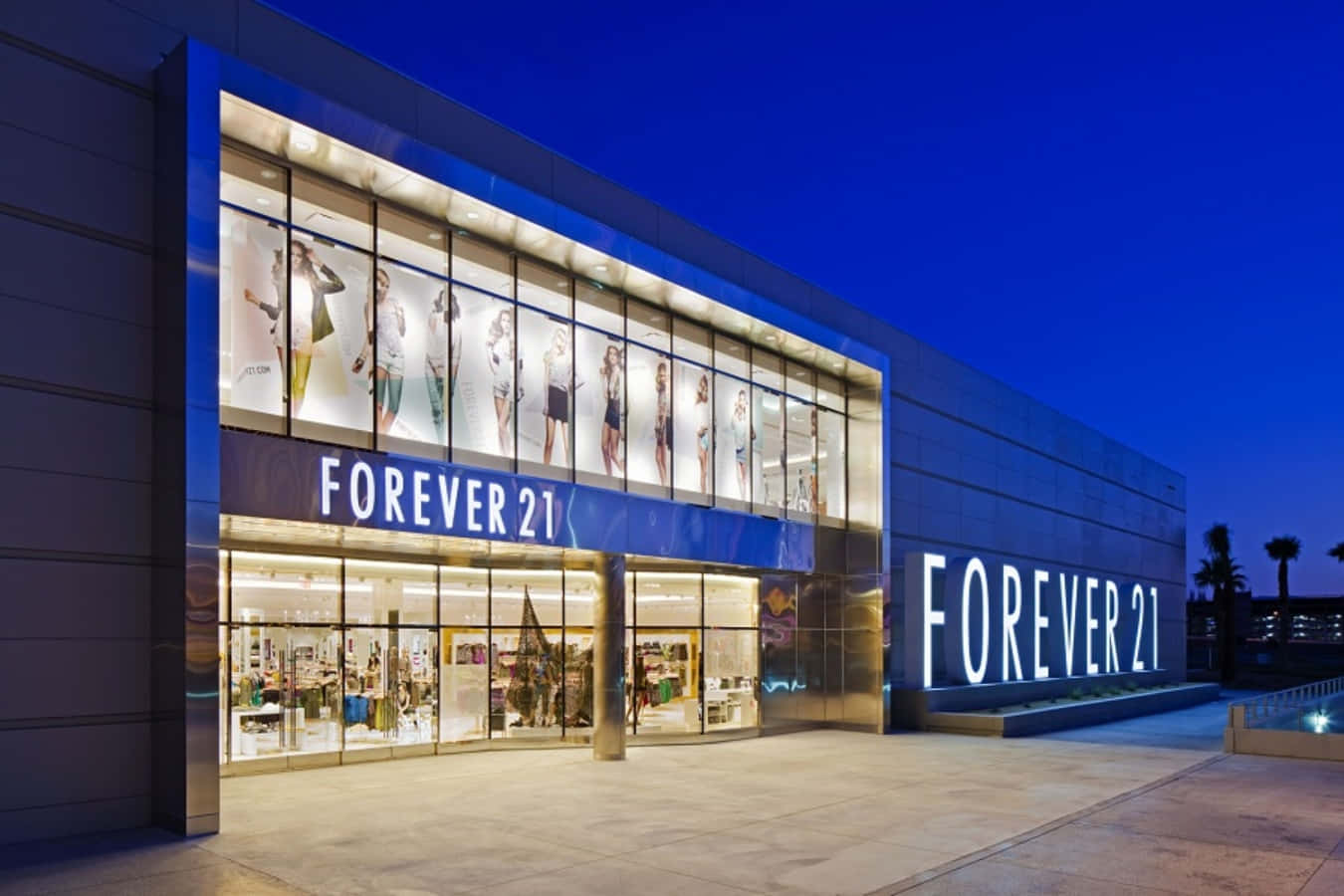 永遠21 桌布 壁紙 — 暮色中燈火通明的Forever 21商店外牆，明亮的櫥窗展示著人體模型和醒目的招牌，襯托著深藍色的天空。