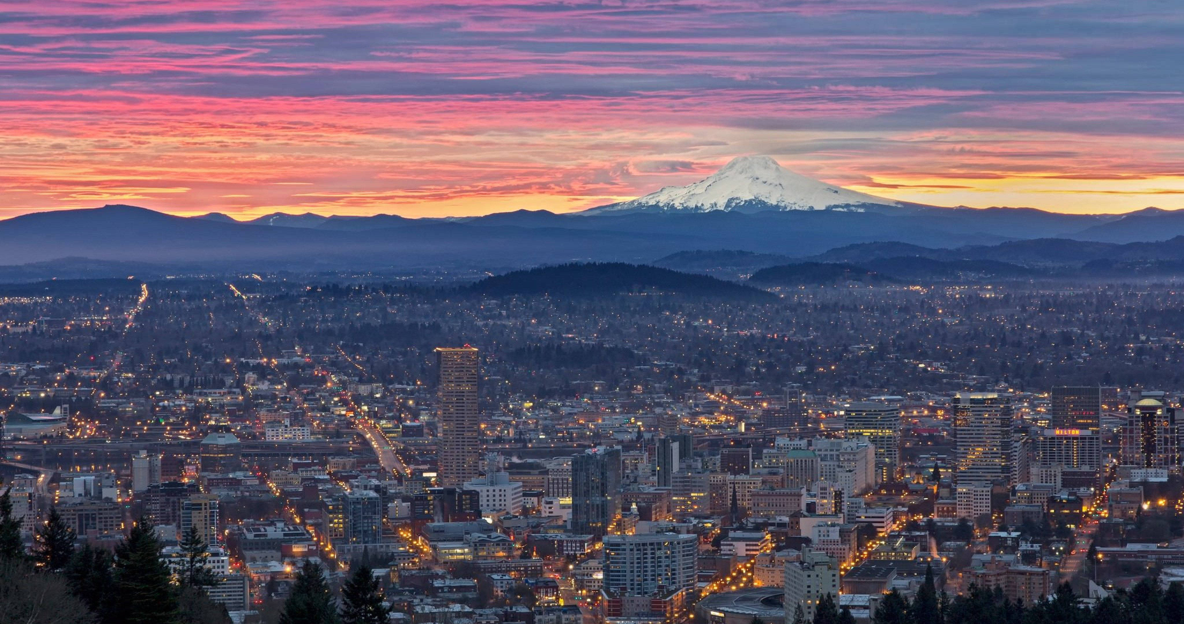 Portland 桌布 壁紙 — 暮色中的城市景觀，一座白雪覆蓋的山峰在粉紅色和橙色的天空下閃耀。