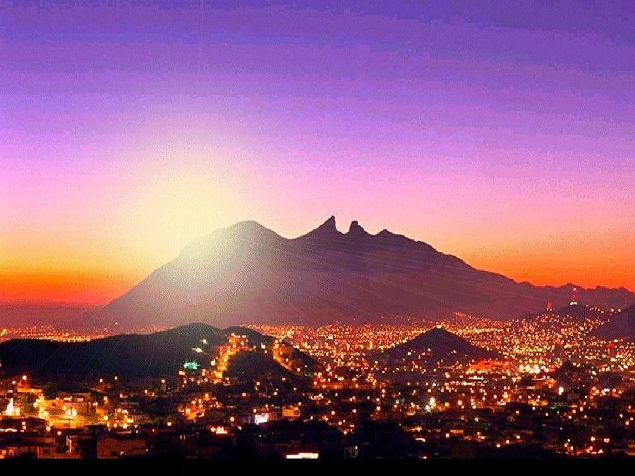 Monterrey 桌布 壁紙 — 暮色中的城市景觀，在雄偉的山脈輪廓下閃爍的燈光，映襯著充滿活力的紫色和橙色天空。