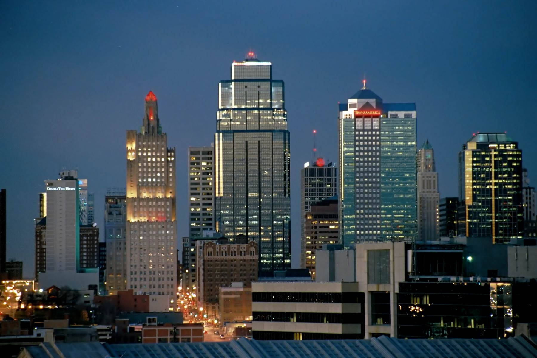Buildings 桌布 壁紙 — 暮色中的城市景觀，摩天大樓燈火通明，窗戶閃爍，映襯著深藍色的天空。