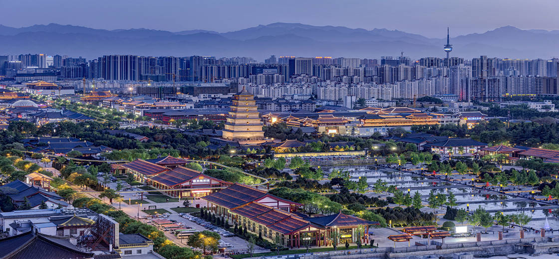 Xian 桌布 壁紙 — 暮色中的城市景觀，融合了古老寶塔和傳統屋頂與現代摩天大樓，背景是霧濛濛的山脈。