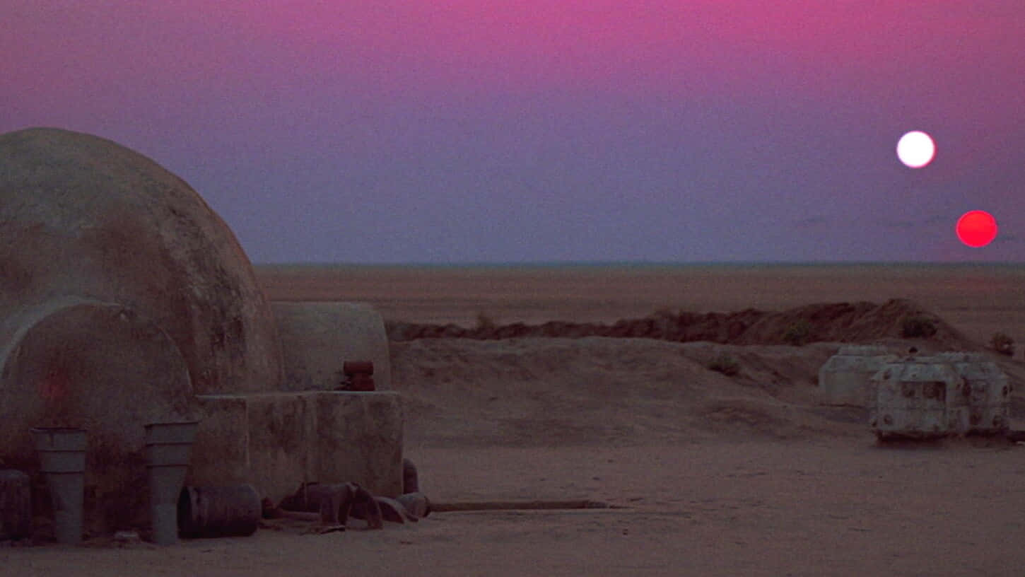 Jakku 桌布 壁紙 — 暮色中的沙漠星球，兩顆太陽在圓頂結構和散落的碎片上方發出粉紅色和紅色的光芒。